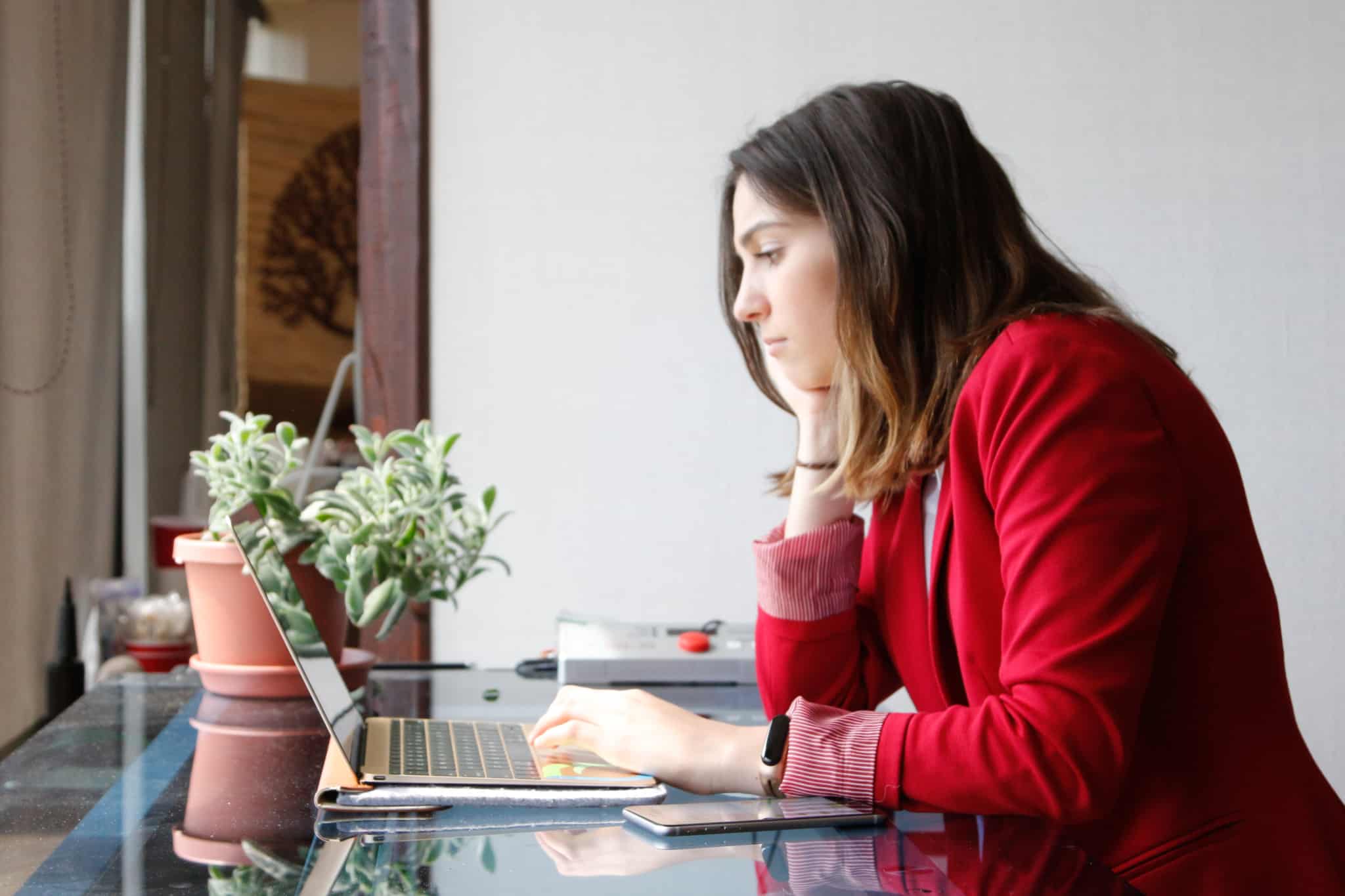 jovem mulher, com ar pensativo e preocupado, ao computador na sua mesa de escritório em casa, prepara entrada no mercado de trabalho