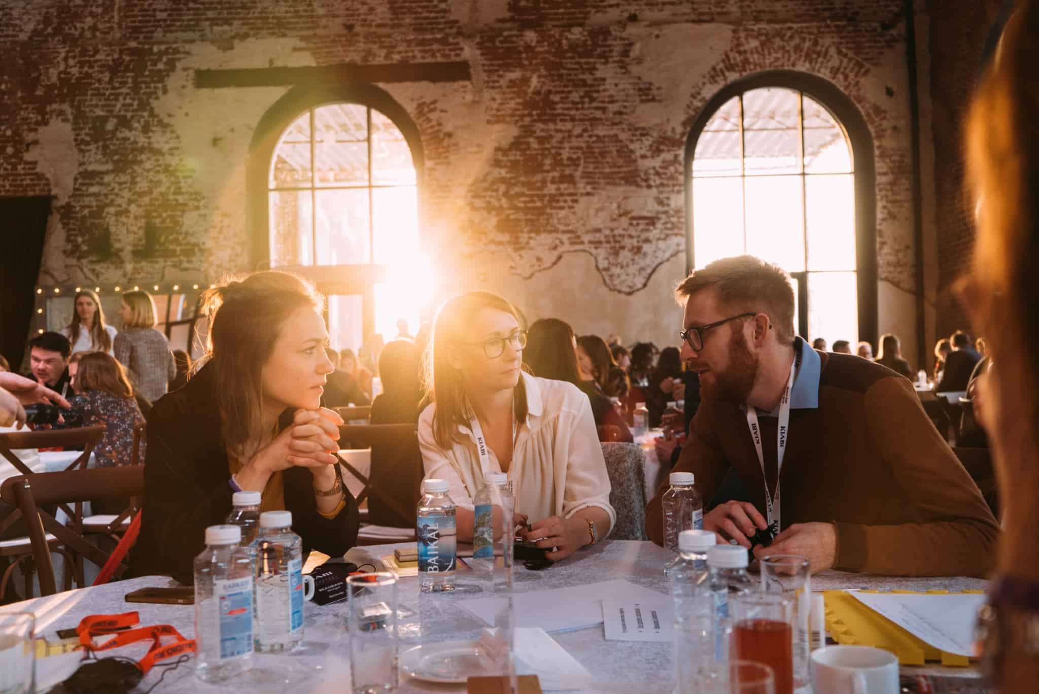 tres jovens, duas mulheres e um homem, sentados a uma mesa de um encontro, a reforçar o networking profissional