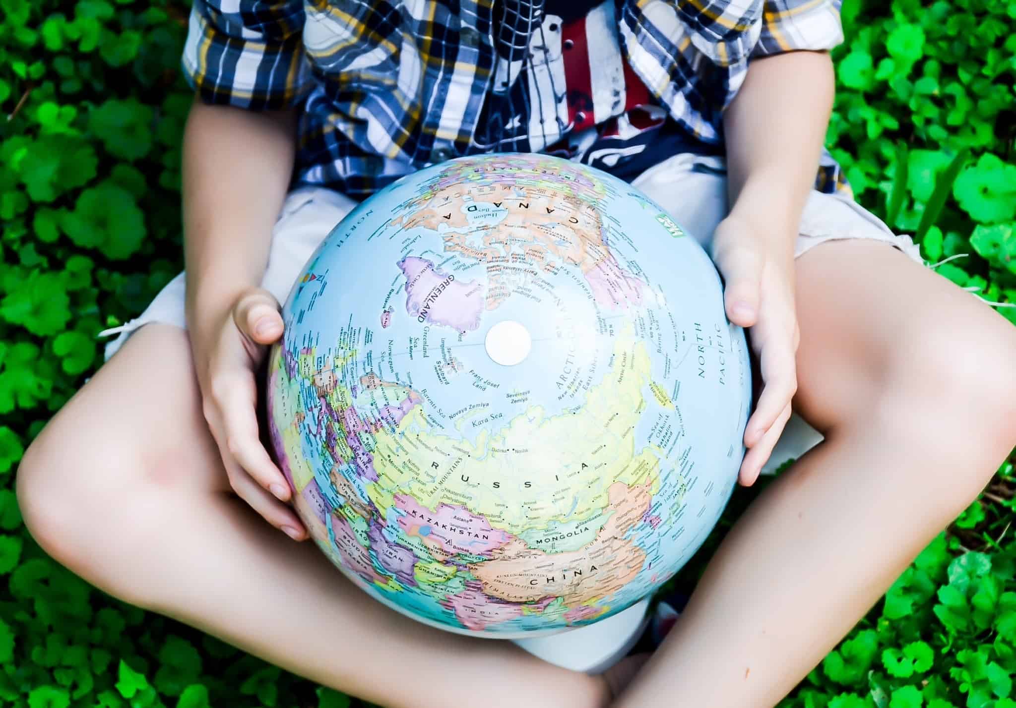 jovem rapaz, sentado na relva bem verde, segura nas mãos, entre as pernas, um globo com o mapa mundo.