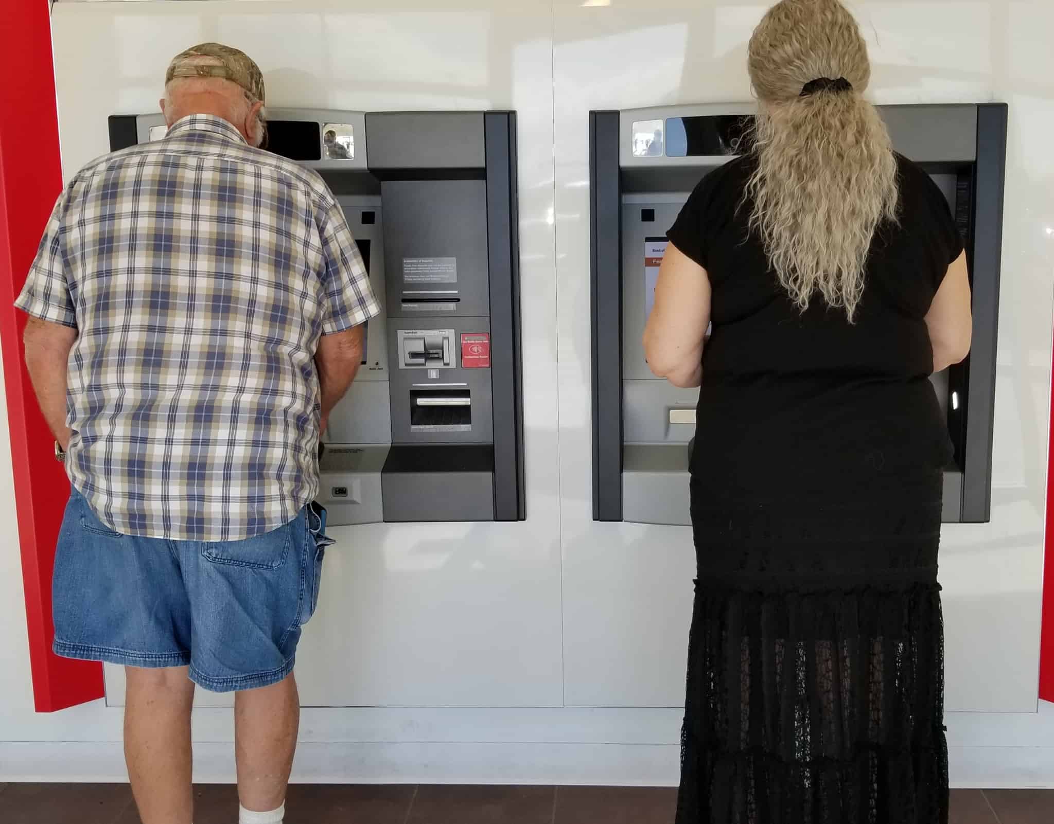 homem e mulher, consultam, separadamente, caixas automáticas, para saber o saldo bancário
