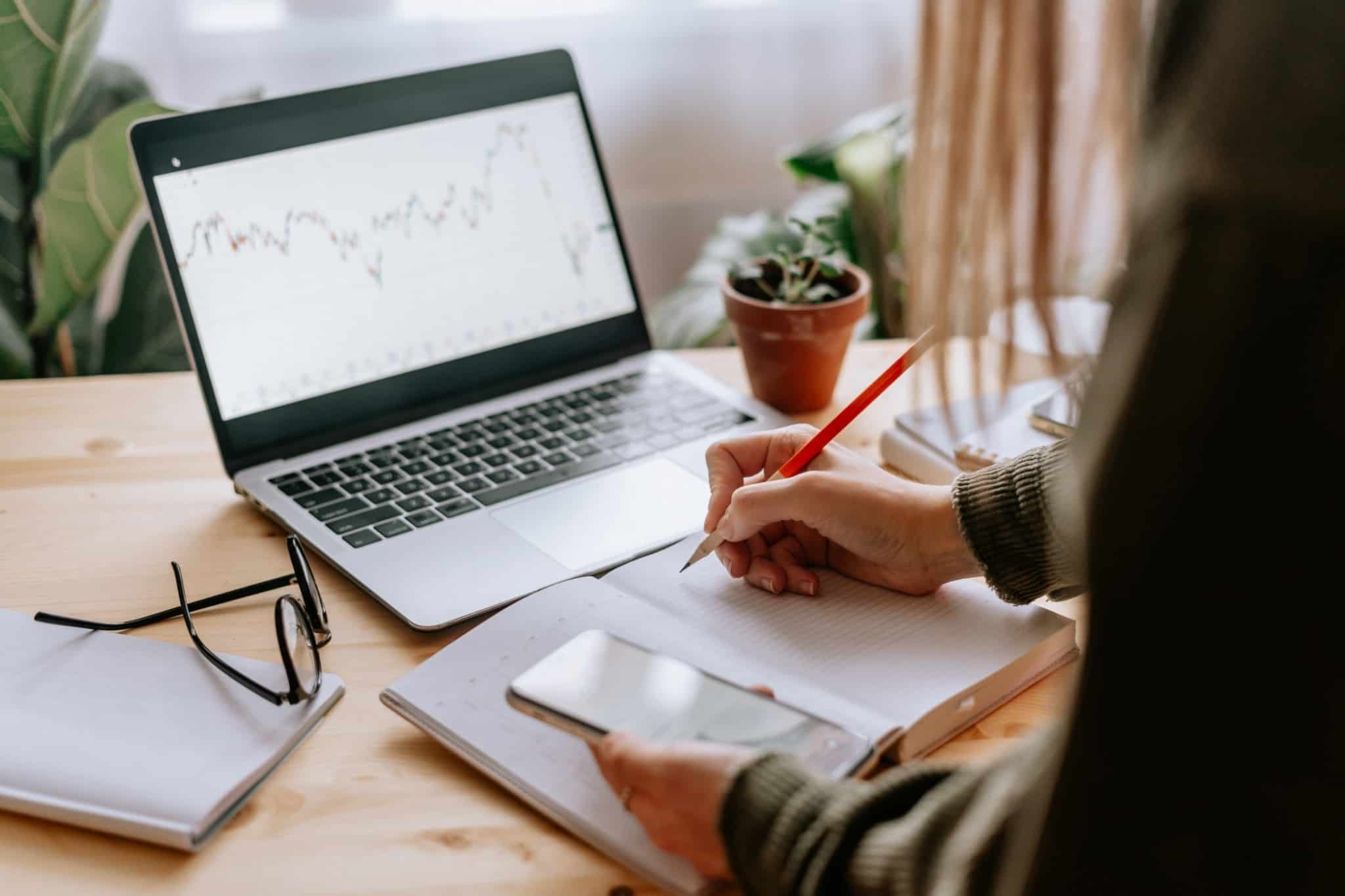 Mulher aponta dúvidas a colocar ao seu intermediário de bolsa sobre o desempenho do seu investimento, observando um gráfico no seu computador.