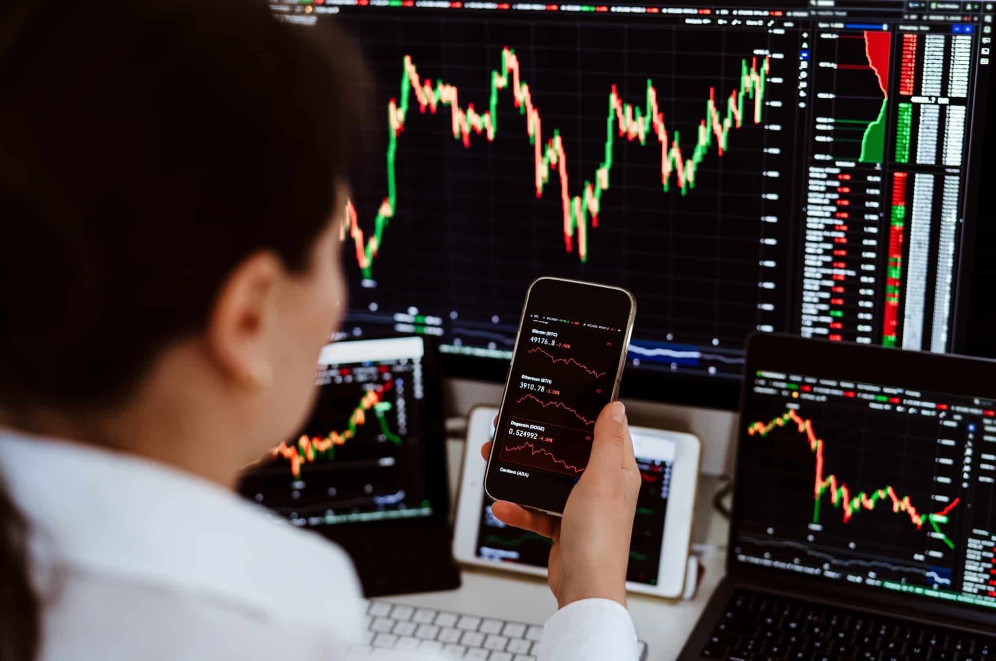 jobem mulher, investidora, analisa gráficos no computador e no telemóvel para acompanhar a evolução das valorizações dos seus investimentos.