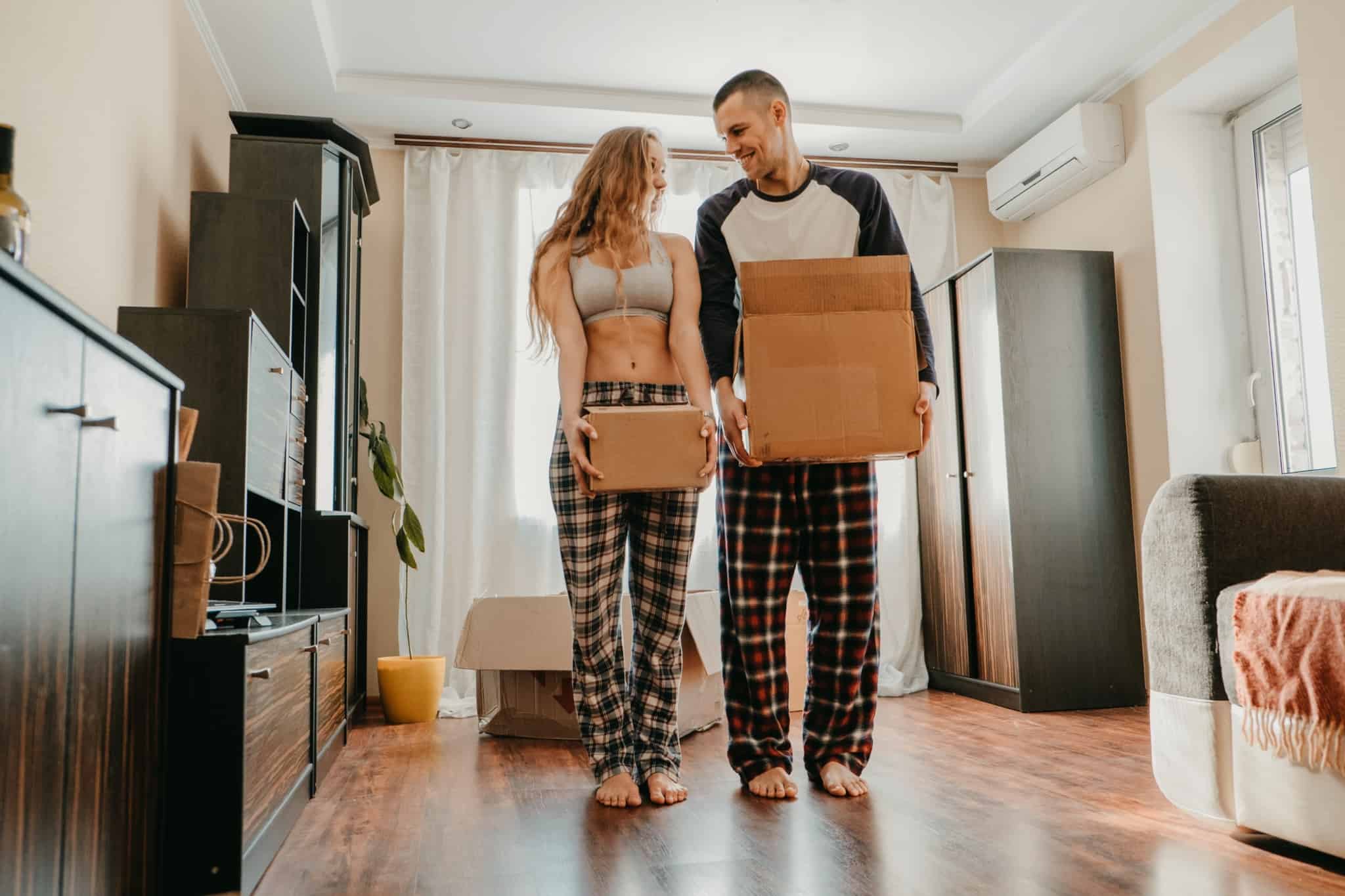 jovem casal, muito sorridente e cúmplice, carrega caixas de cartão de arrumação porque vão mudar de casa