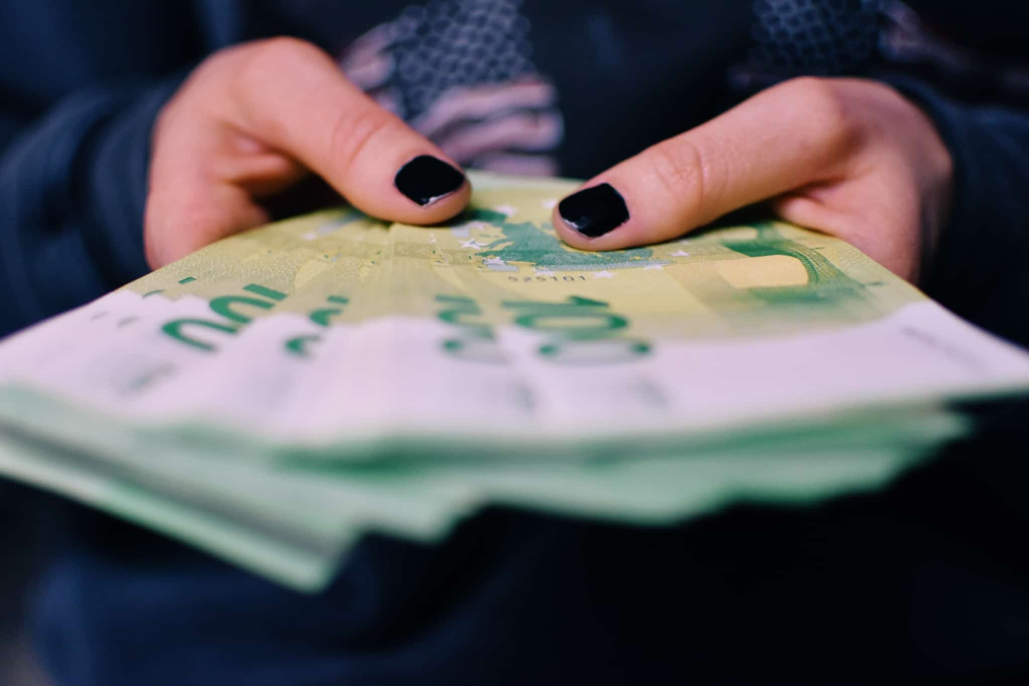 produção fotográfica que mostra as mãos de uma jovem mulher a segurar um moljo de notas de 100 euros, ilustra o pagamento em dinheiro (numerário)