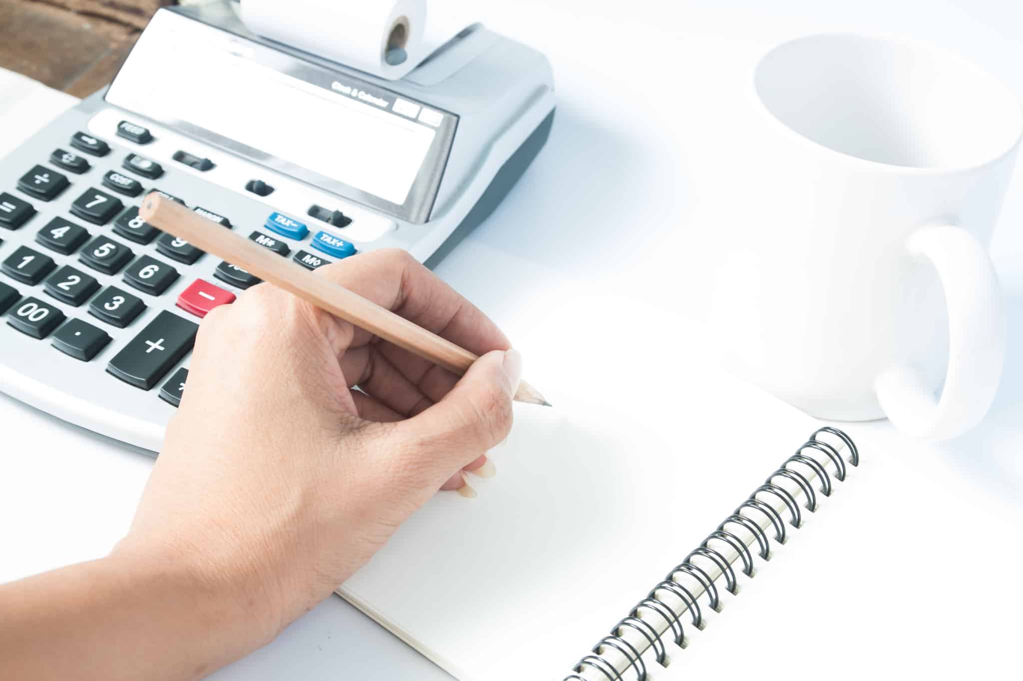 diferença entre poupar ou investir ilustrada com uma calculadora e um bloco a ser usado por alguém, mas vê-se apenas a mão
