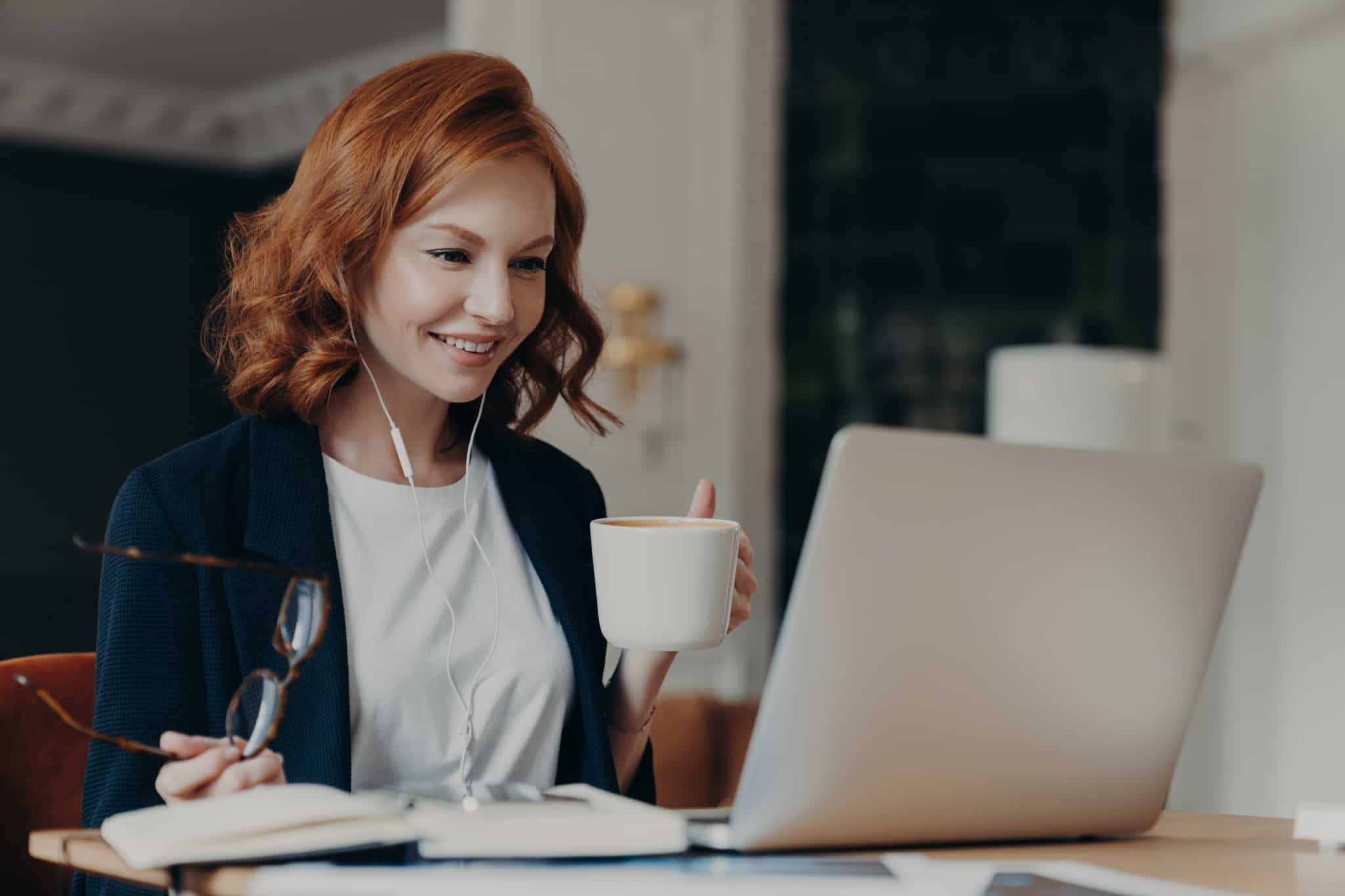 jovem mulher ao computadoir a trabalhar , sorridente e com um ar tranquilo, enquanto bebe um cafe