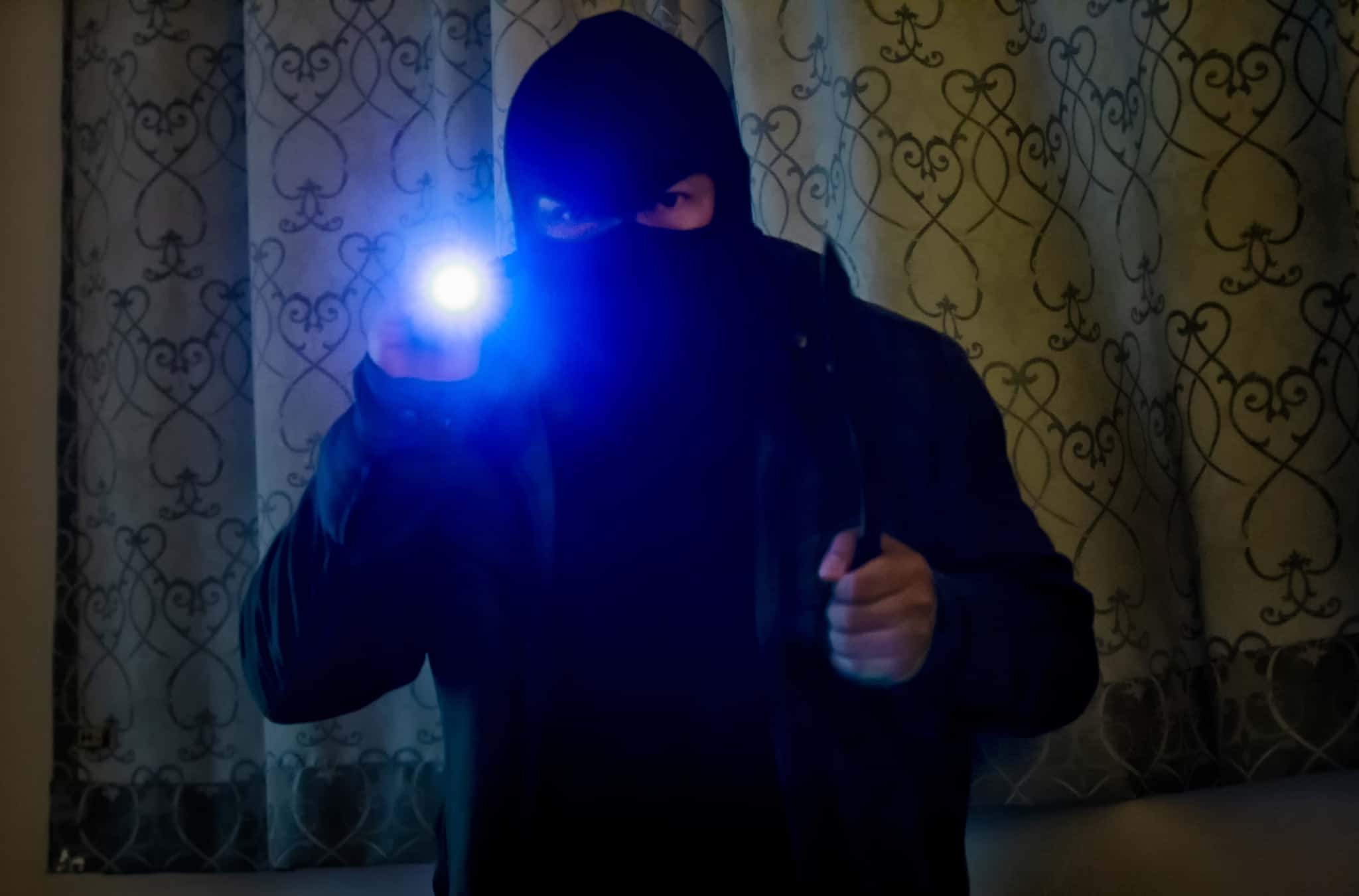 assaltante, encapuçado, a entrar numa casa durante a noite e de lanterna na mão
