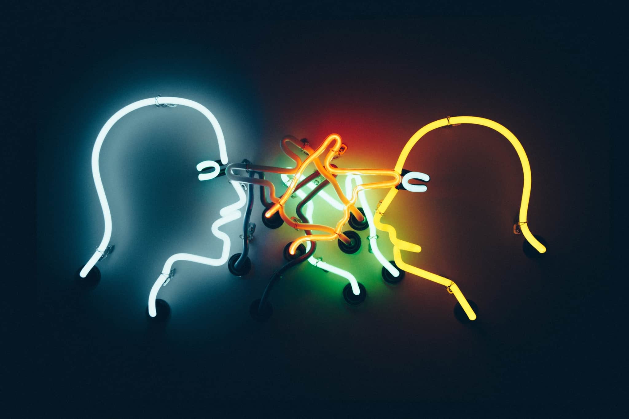 produção fotográfica ilustra o bullying imobiliário com duas cabeças , em neon, de homens que discutem e apontam o dedo