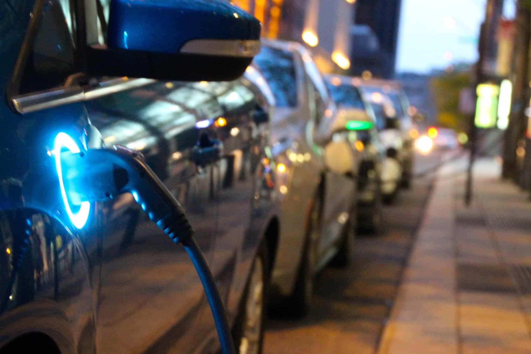 carro elétrico, entre uma fila longa de carros estacionados, está a carregar num posto de abastecimento