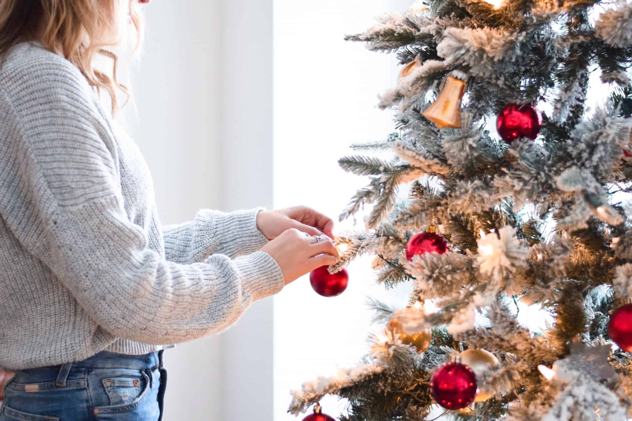 jovem mulher decora a sua árvore de Natal com bolas vermelhas e sinos dourados