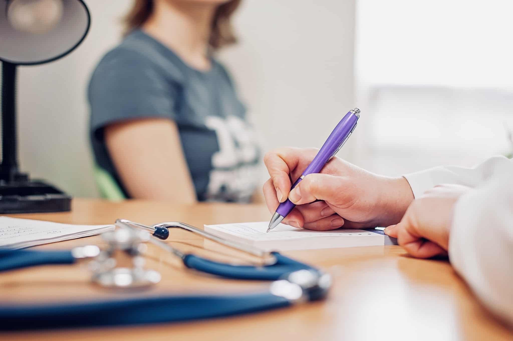 jovem mulher em consulta médica aguarda a prescrição que o médico está a redigir