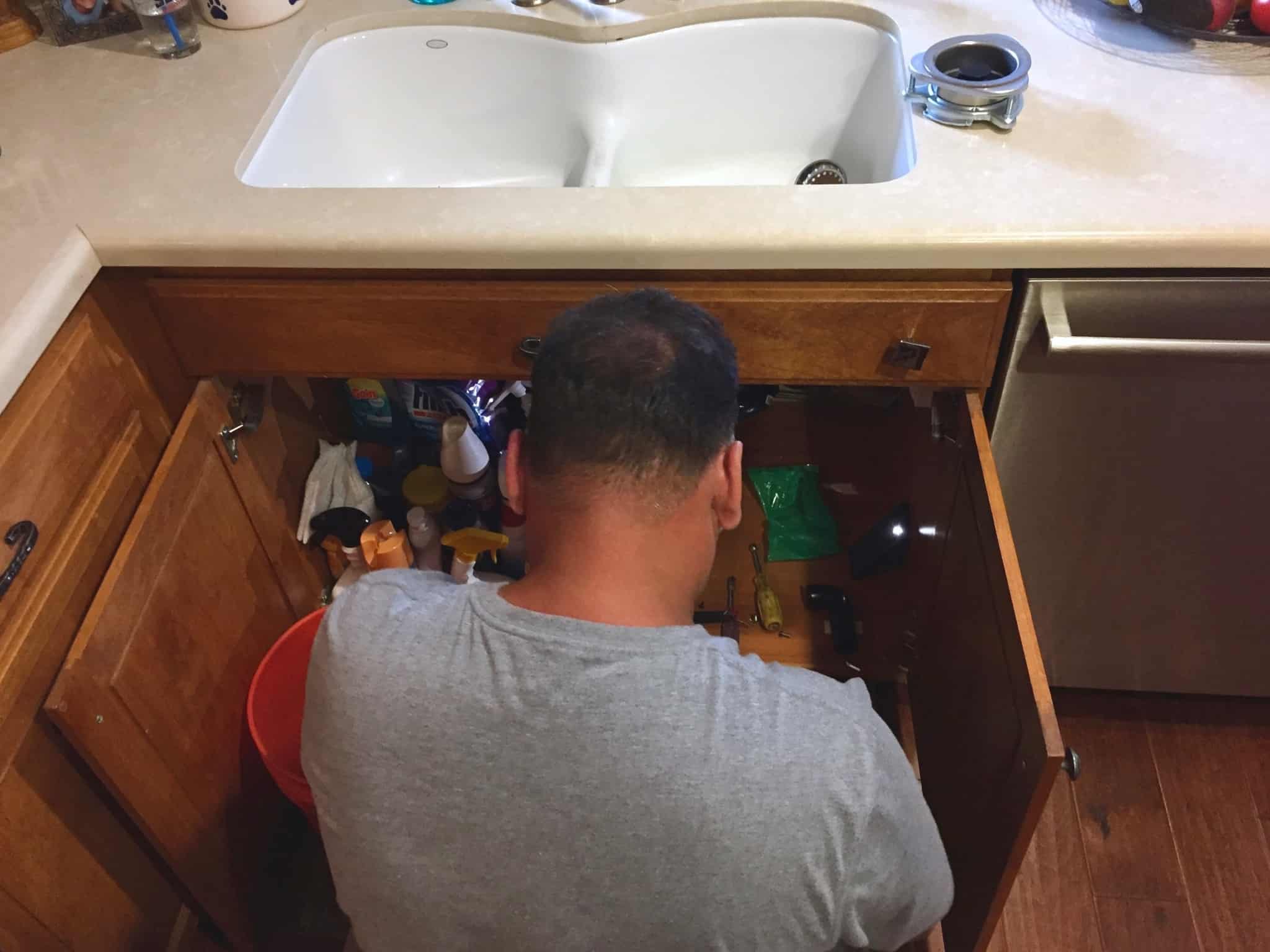 homem, a trabalhar por debaixo do lava-louça, tenta arranjar canos. Sáo obras que podem ter de ser feitas poelo senhorio, dependendo da gravidade