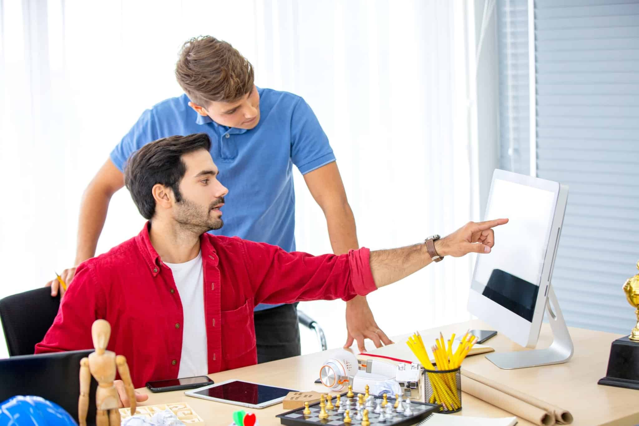 Dois homens partilham ideias no escritório, em frente de um computador