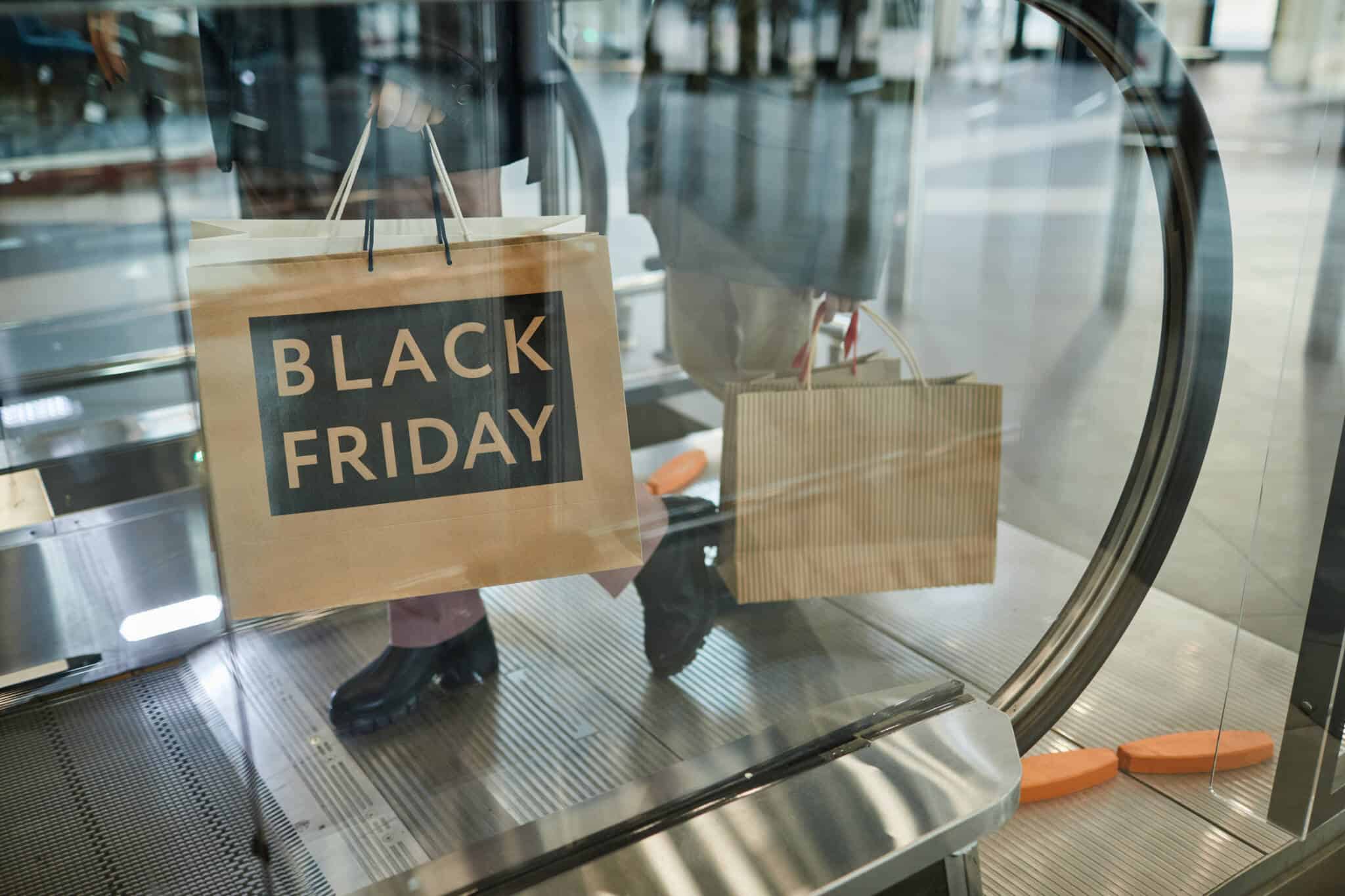 homem carrega sacos de compras feitas na Black Friday, circulando nas escadas rolantes de um centro comercial