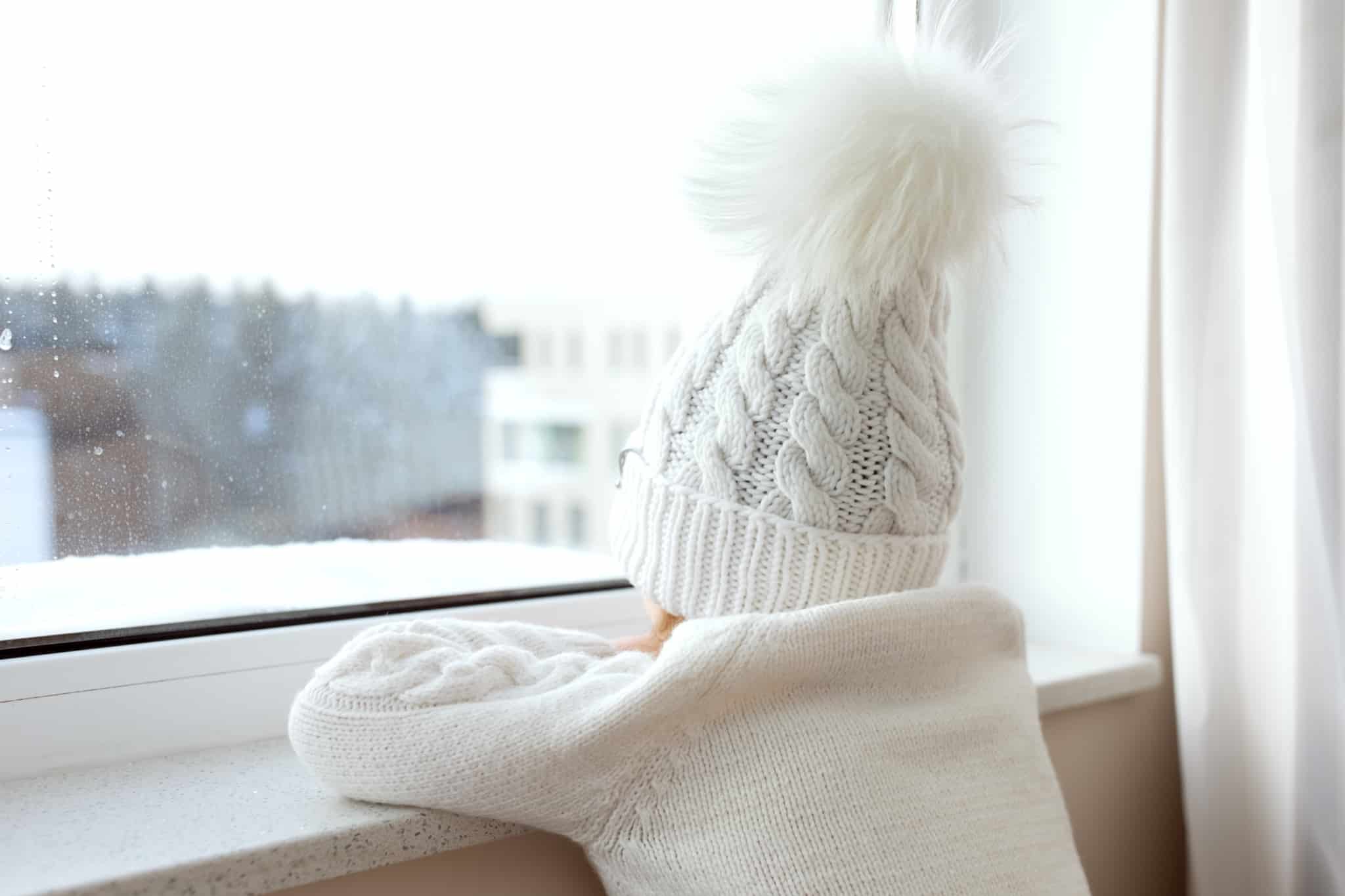 criança com um gorro na cabeça a espreitar à janela