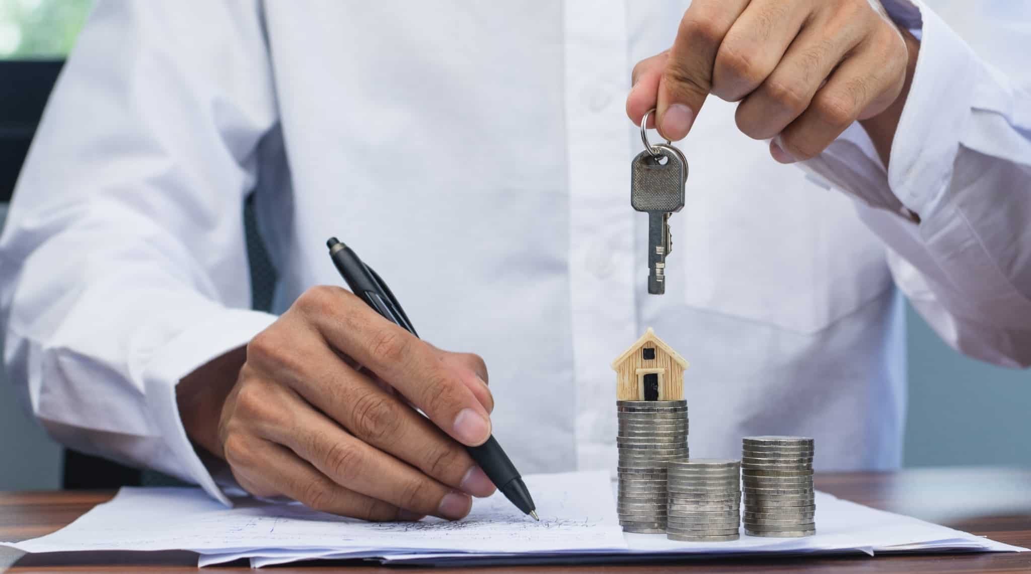Homem a segurar uma chave de casa com uma caneta para assinar os papéis na outra mão