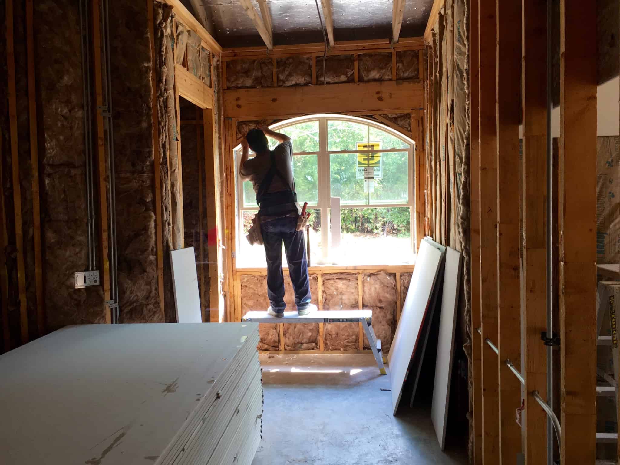 homem a construir o interior de uma casa, trabalha junto a uma janela