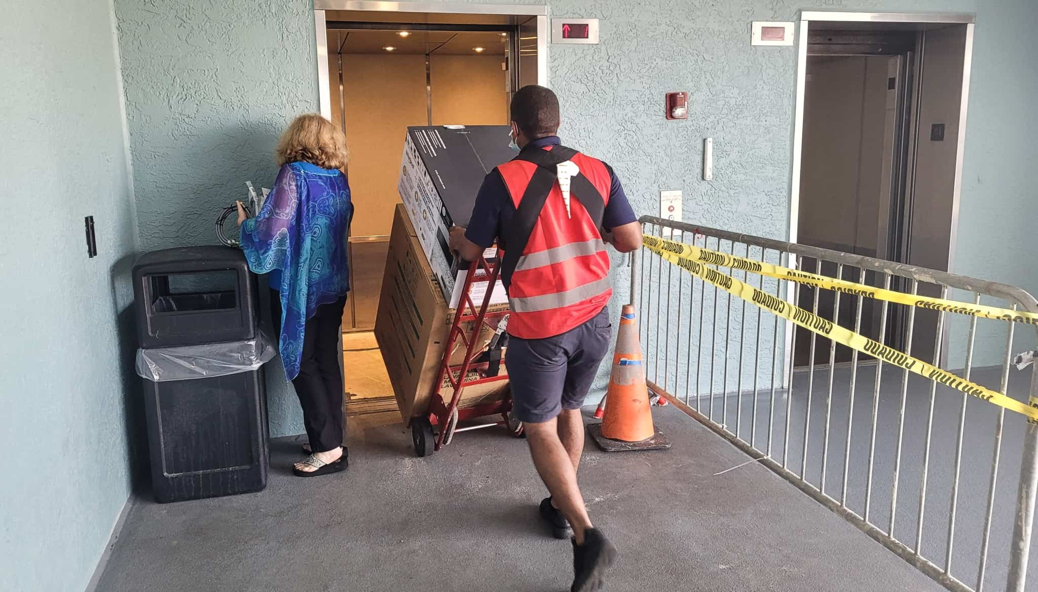 homem a entrar no elevador levando num carrinho um frigorífico, novo ainda empacotado