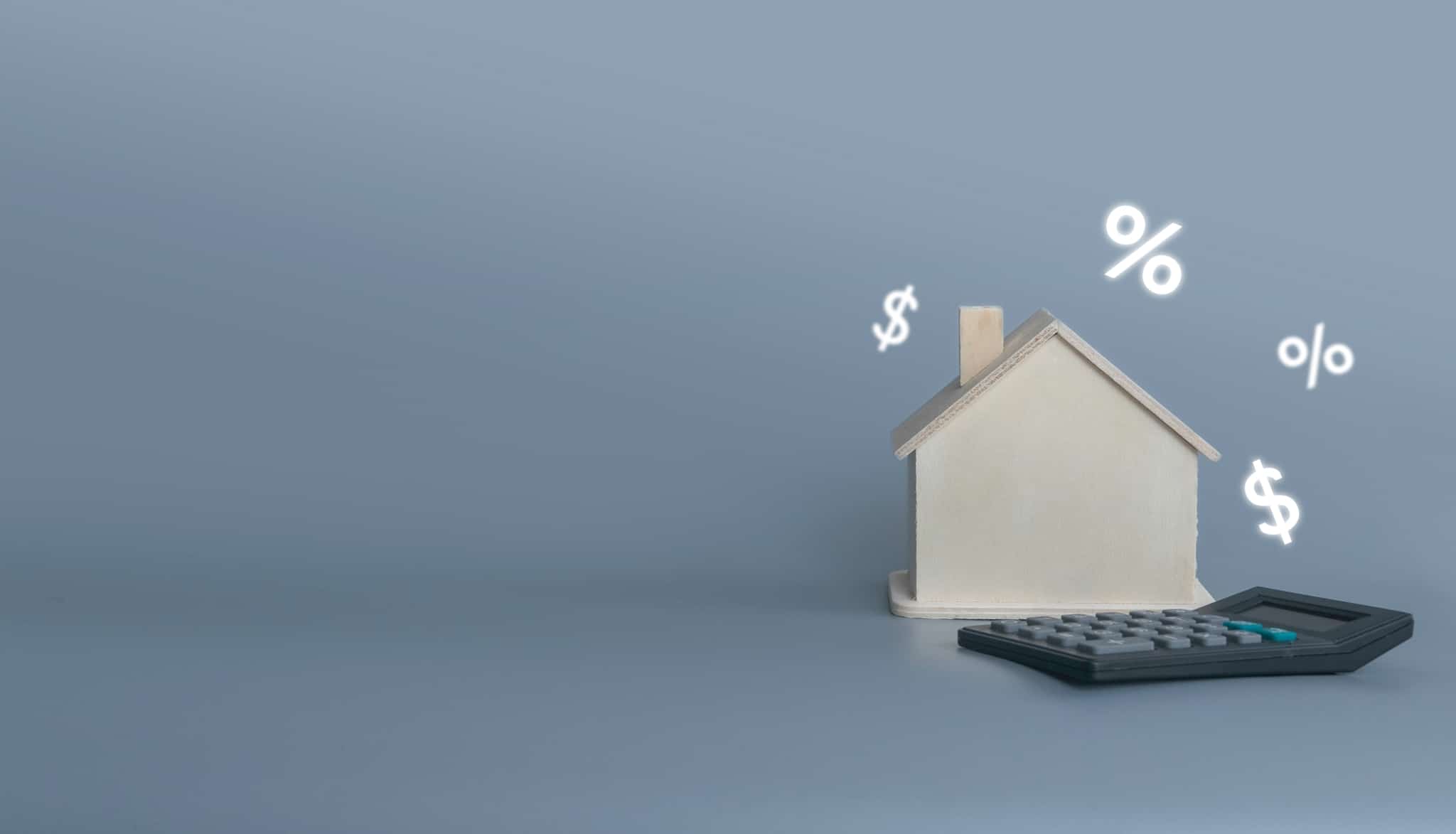 produção fotográfica mostra apenas uma casa rodeada por vários símbolos financeiros e acompnhada de uma calculadora