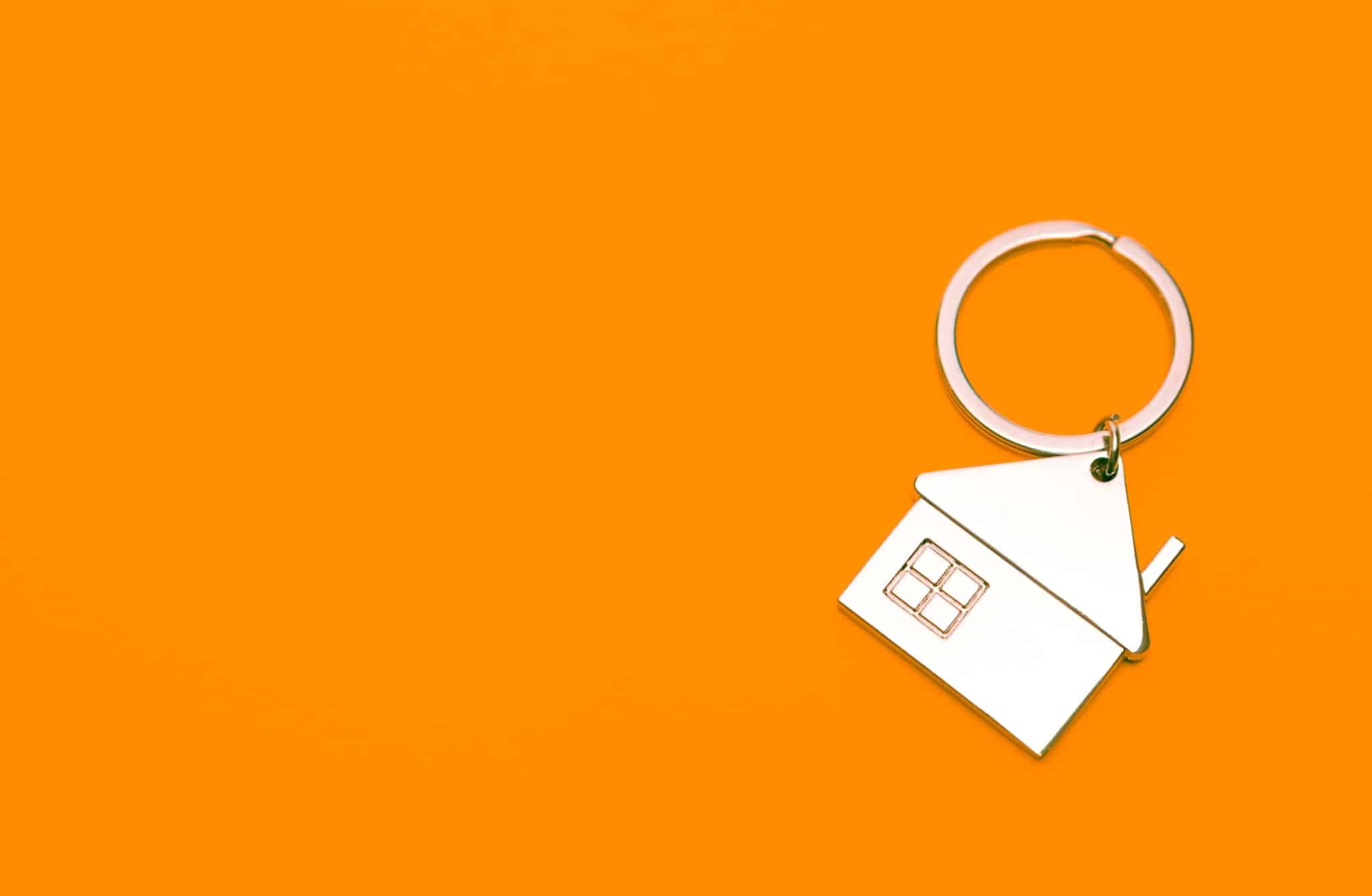 uma produção fotográfica ilustra o tema do imóvel do banco só com um porta chaves com uma casa em fundo laranja