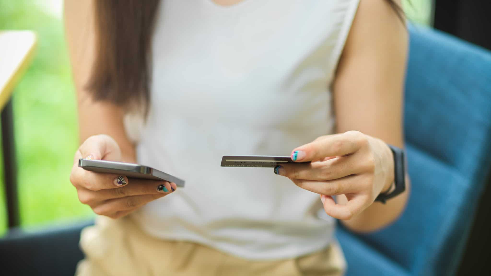 jovem mulher segira cartão de crédito e telemóvel que está a usar para fazer um pagamento