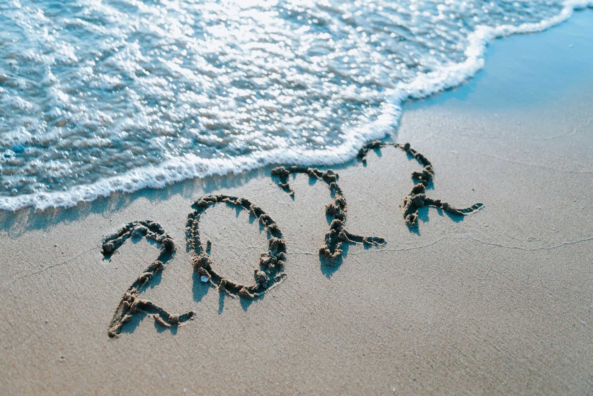 2022 escrito na areia da praia, junto ao mar, com a espuma de uma onda a aproximar-se