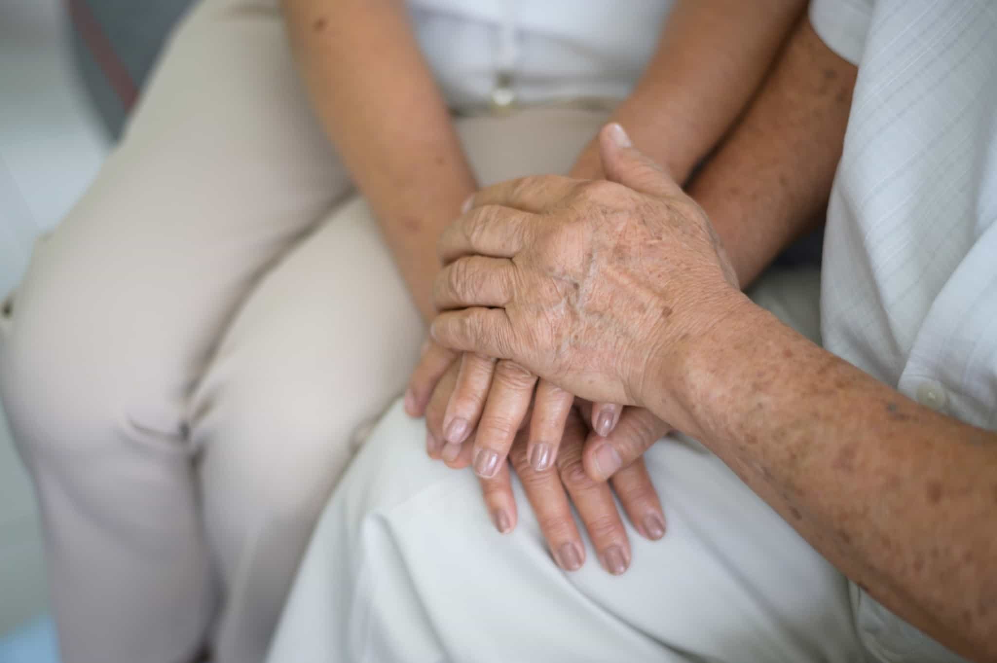 Imagem de duas pessoas de diferentes idades com as mãos sobrepostas - cuidador informal