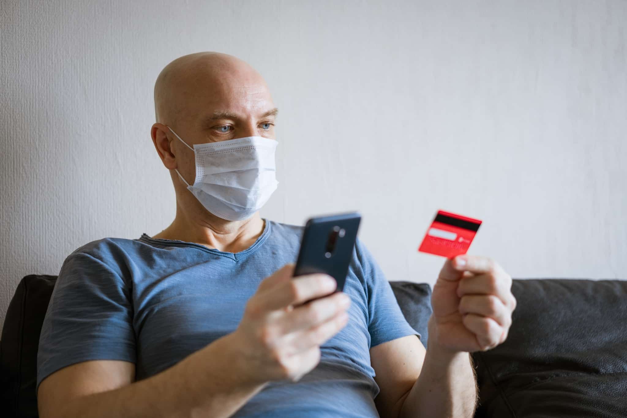 Homem com máscara a segurar cartão de crédito e telemóvel a fazer um seguro de proteção