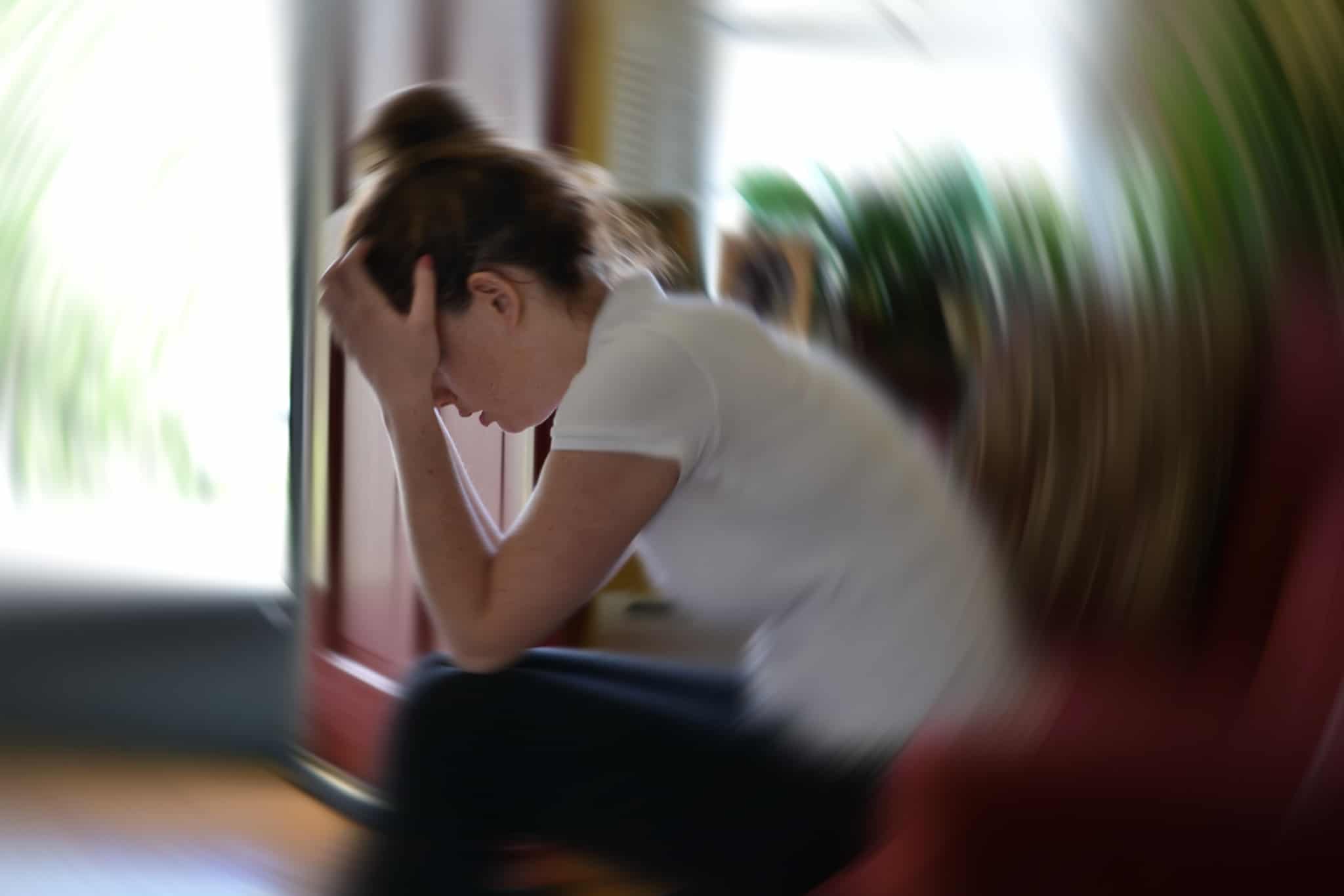 uma jovem mulher, sentada no sofá em casa, preocupada e desorientada, chora o falecimento de um familiar