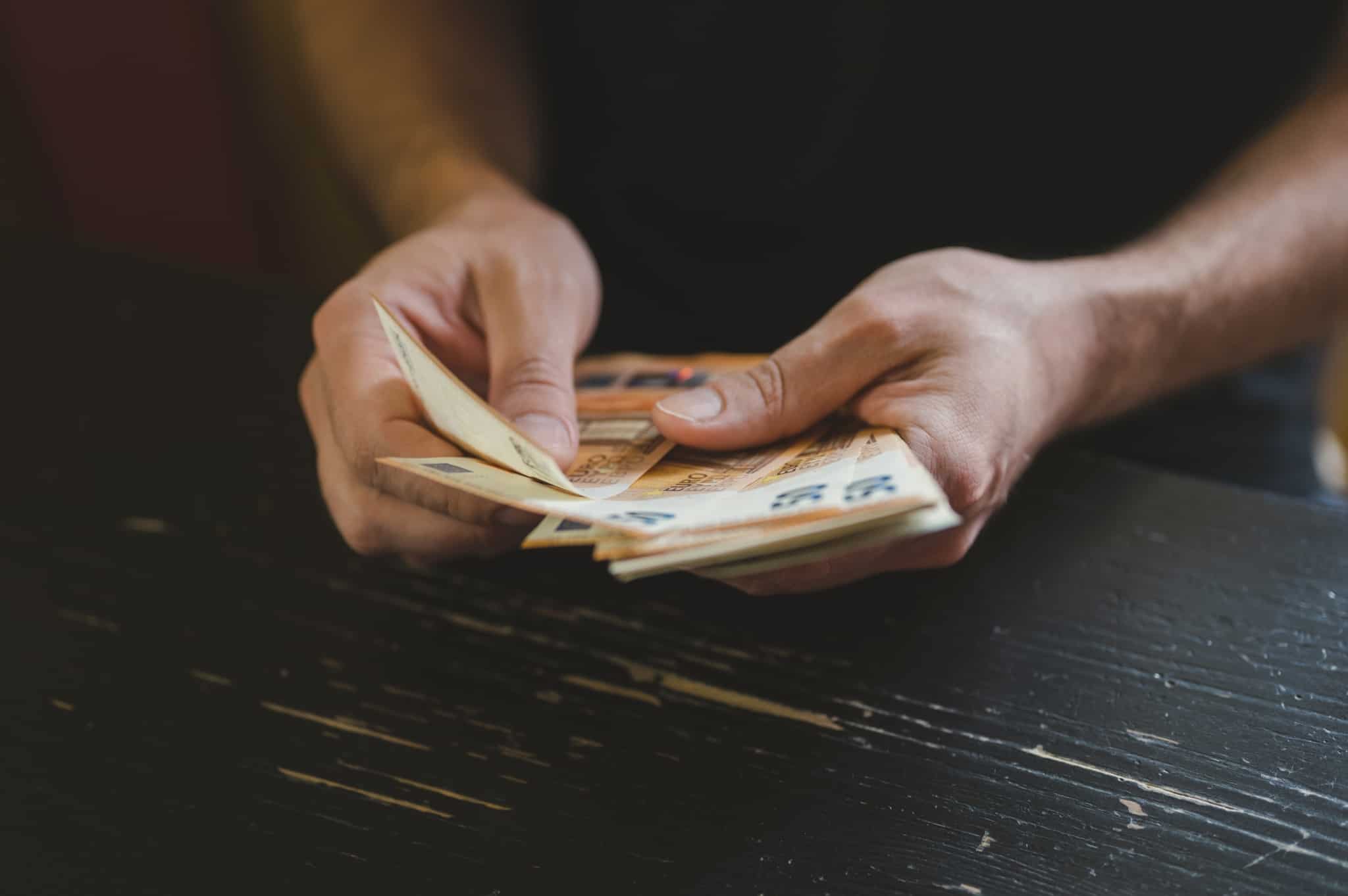 produção fotográfica deixa apenas ver as mãos de um homem jovem que conta um molho de notas de 50 euros