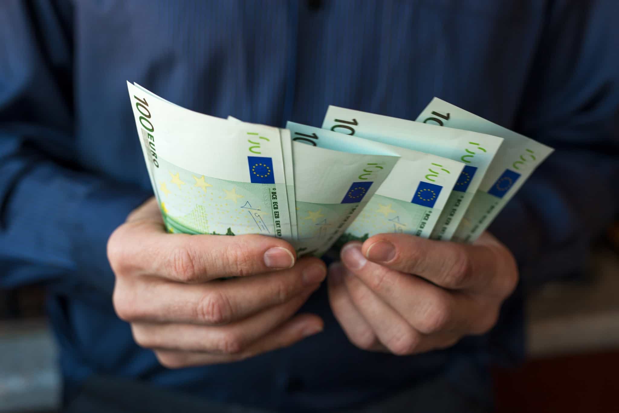 homem segura e conta um molho de notas de 100 euros