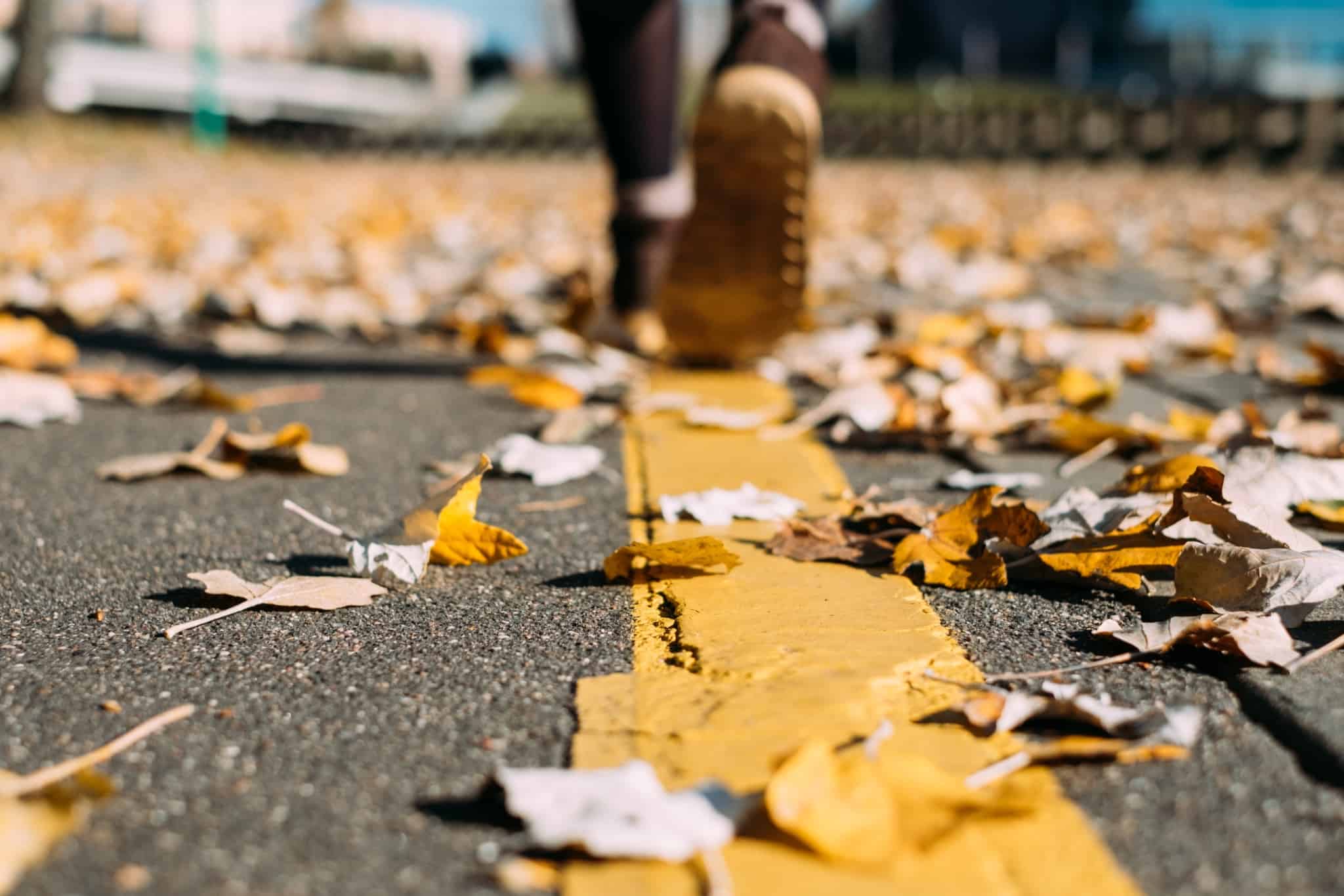 pés de um jovem a caminhar pela estadra repleta de folhas das árvores, amarelas, típicas do outono e inverno