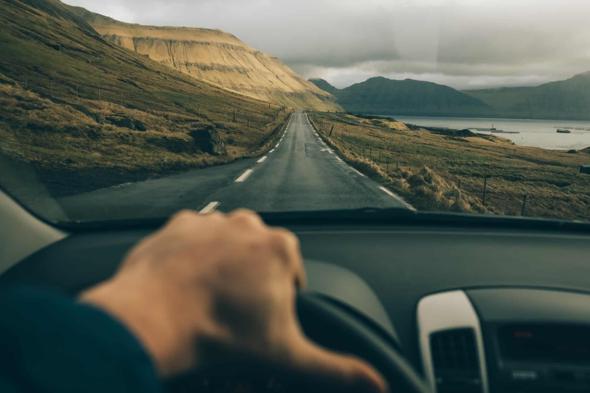 mão no volante de um automóvel que percorre uma estrada longa no meio da natureza