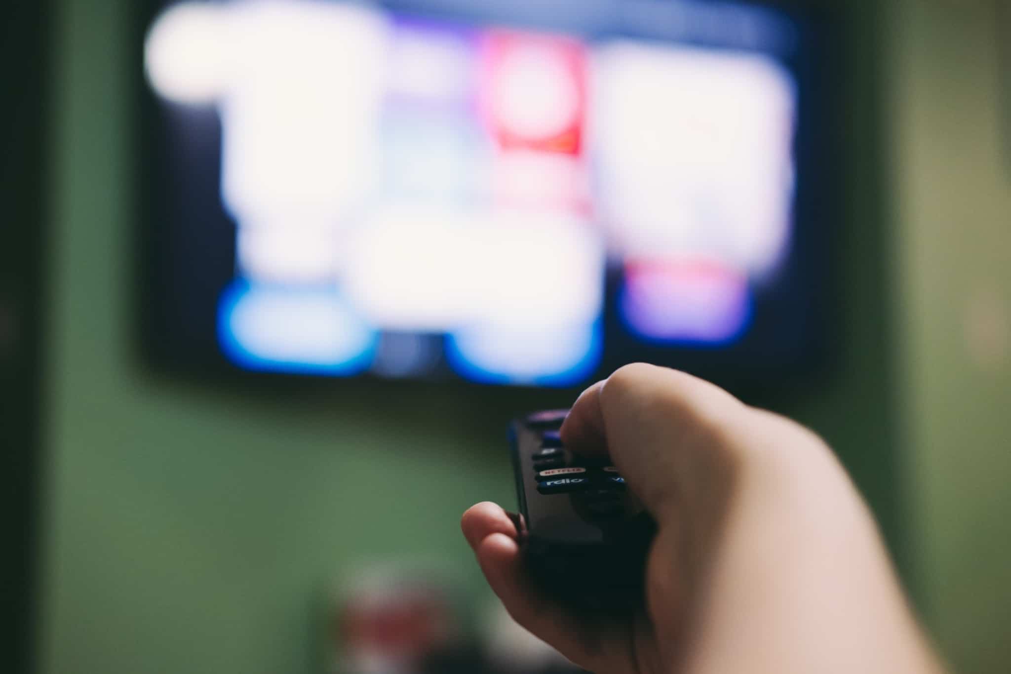 ecran de TV desfocado com vários serviços streaming. Mão aponta o comando para a TV