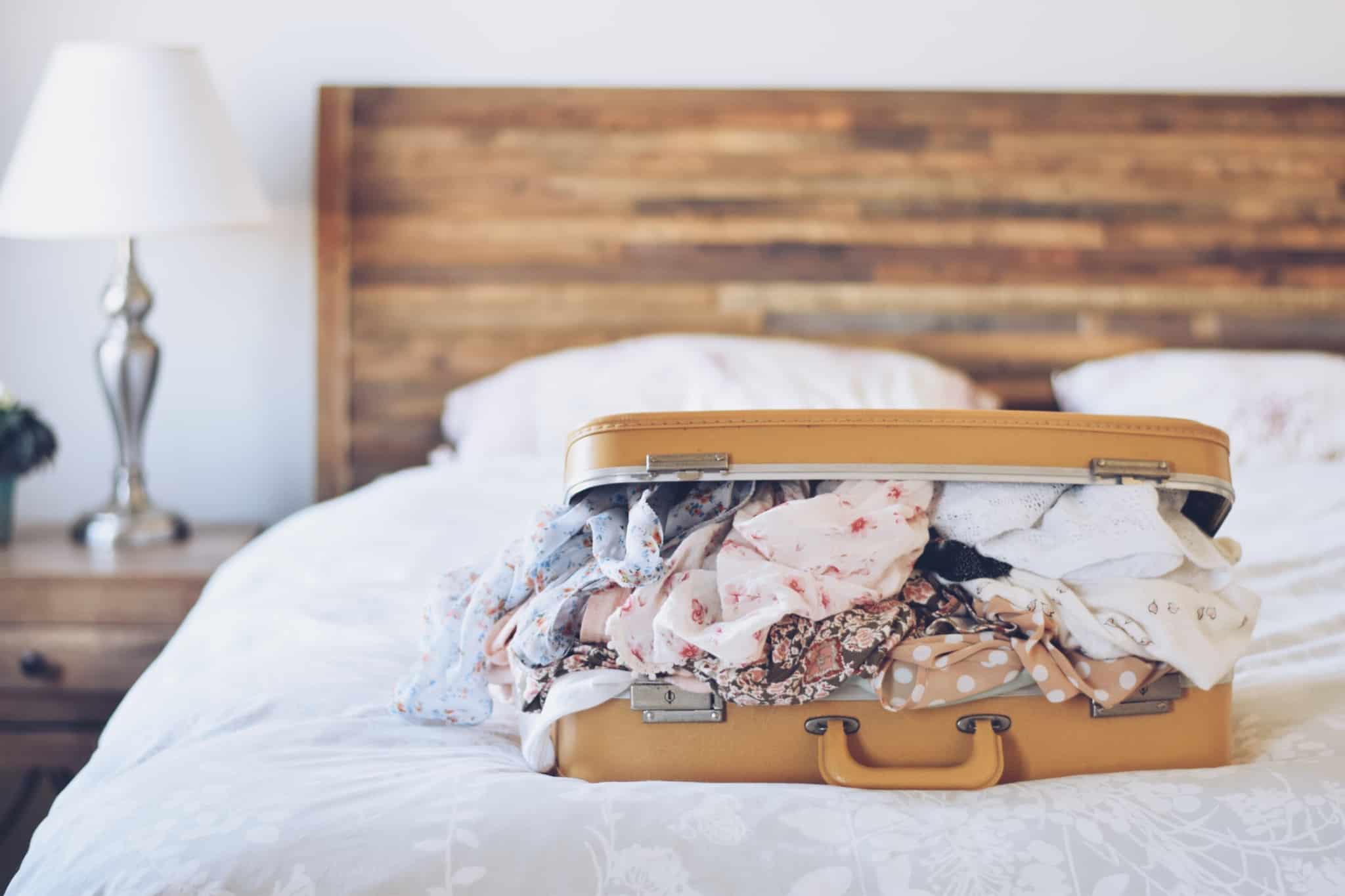 Cama de quarto com mala de viagem aberta com roupa por cima