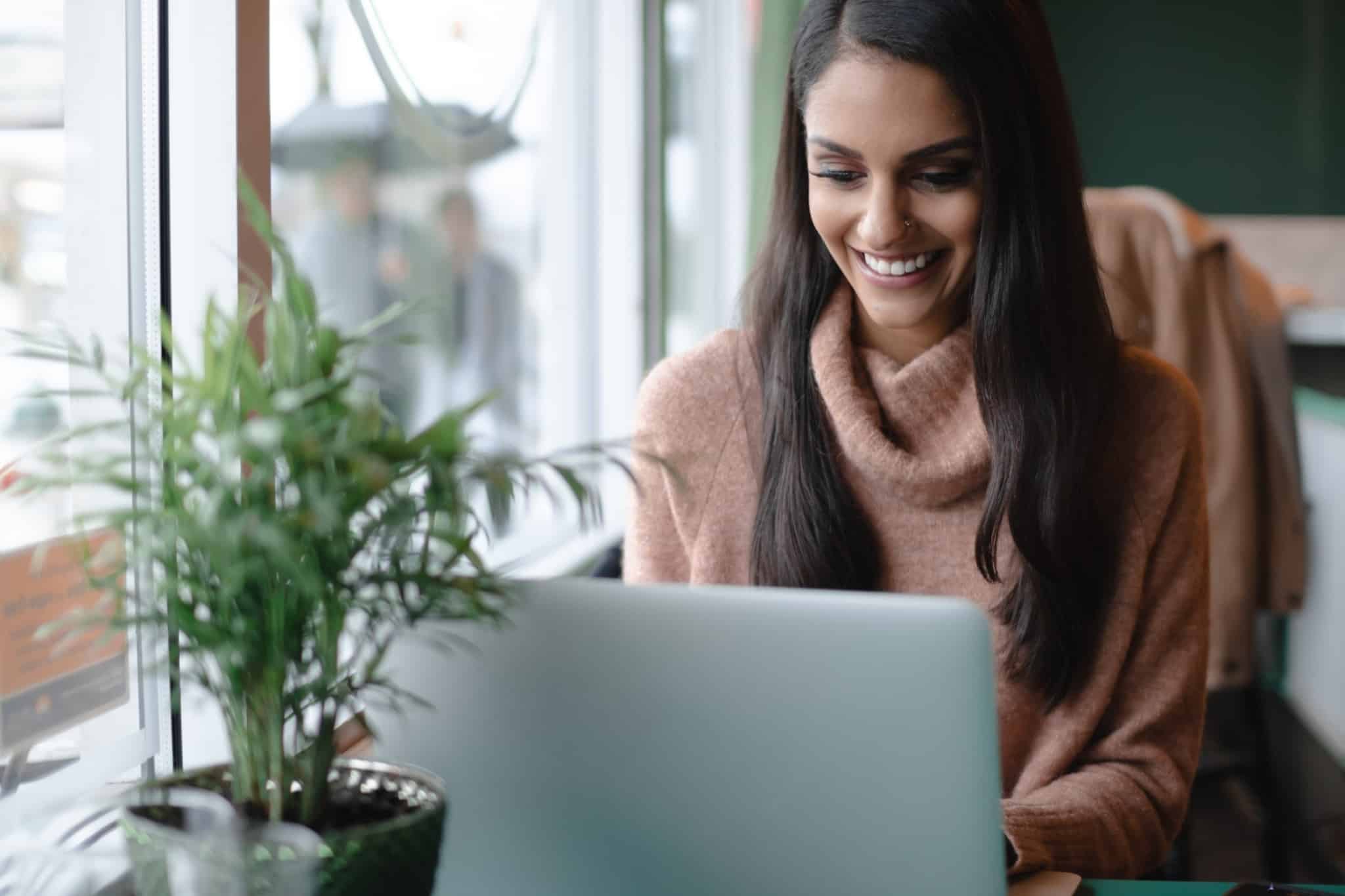 Mulher sentada ao computador, de sorriso rasgado, enquanto trabalha