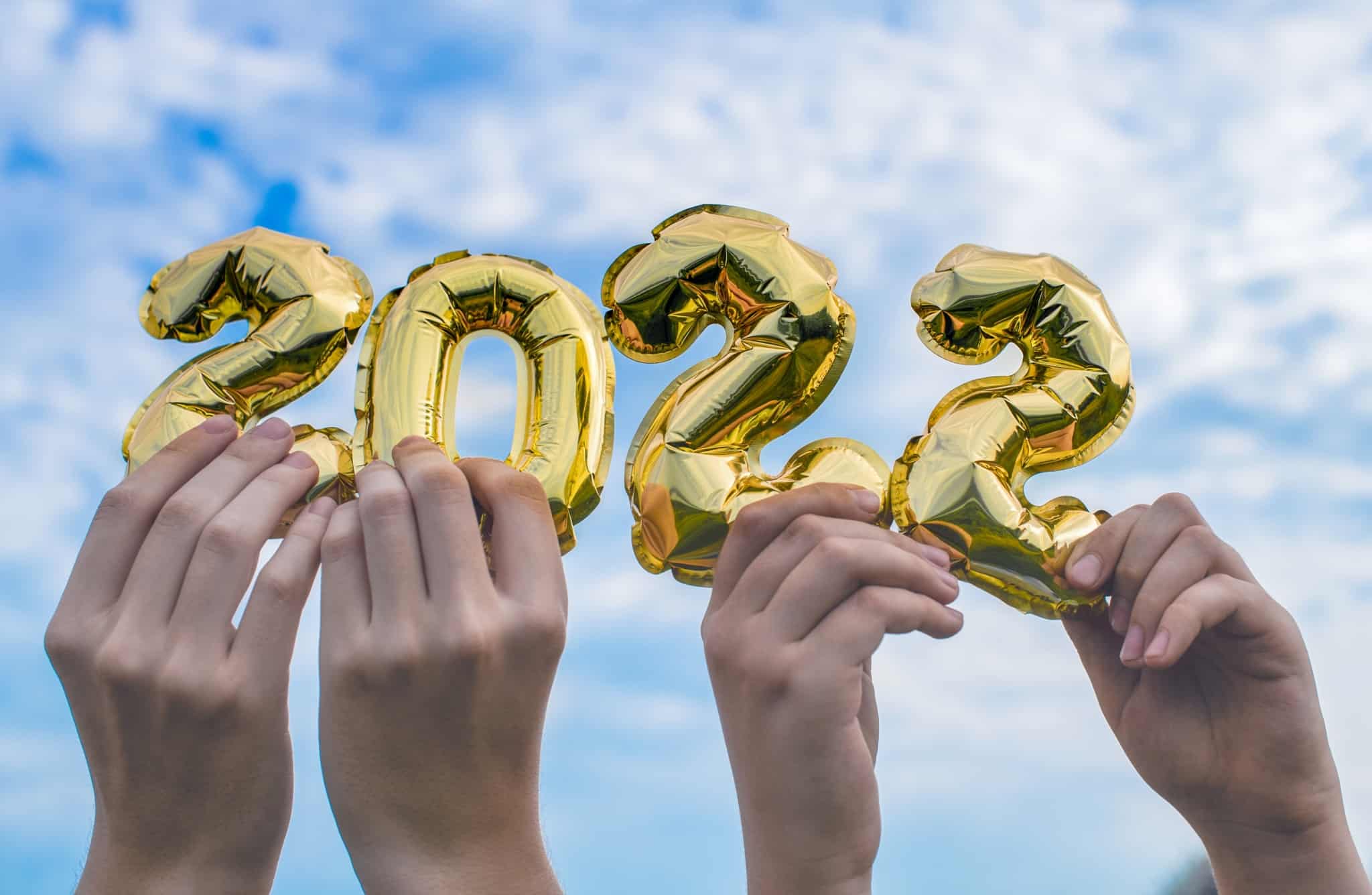 quatro mãos erguem ao céu balões dourados com números individuais que perfazem o novo ano de 2022