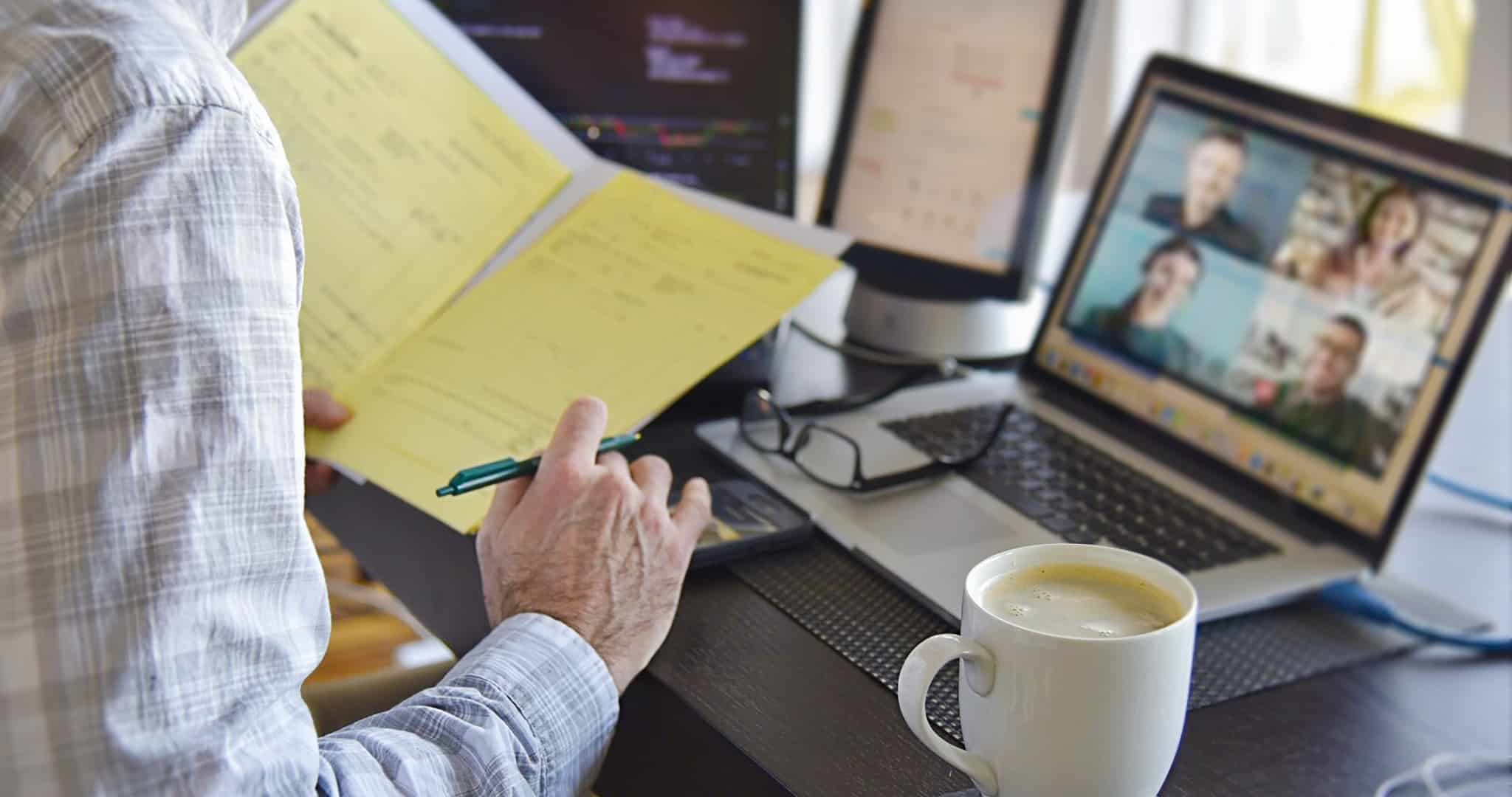 Costas de senhor, trabalhador independente, ao computador em reunião e a pegar num caderno