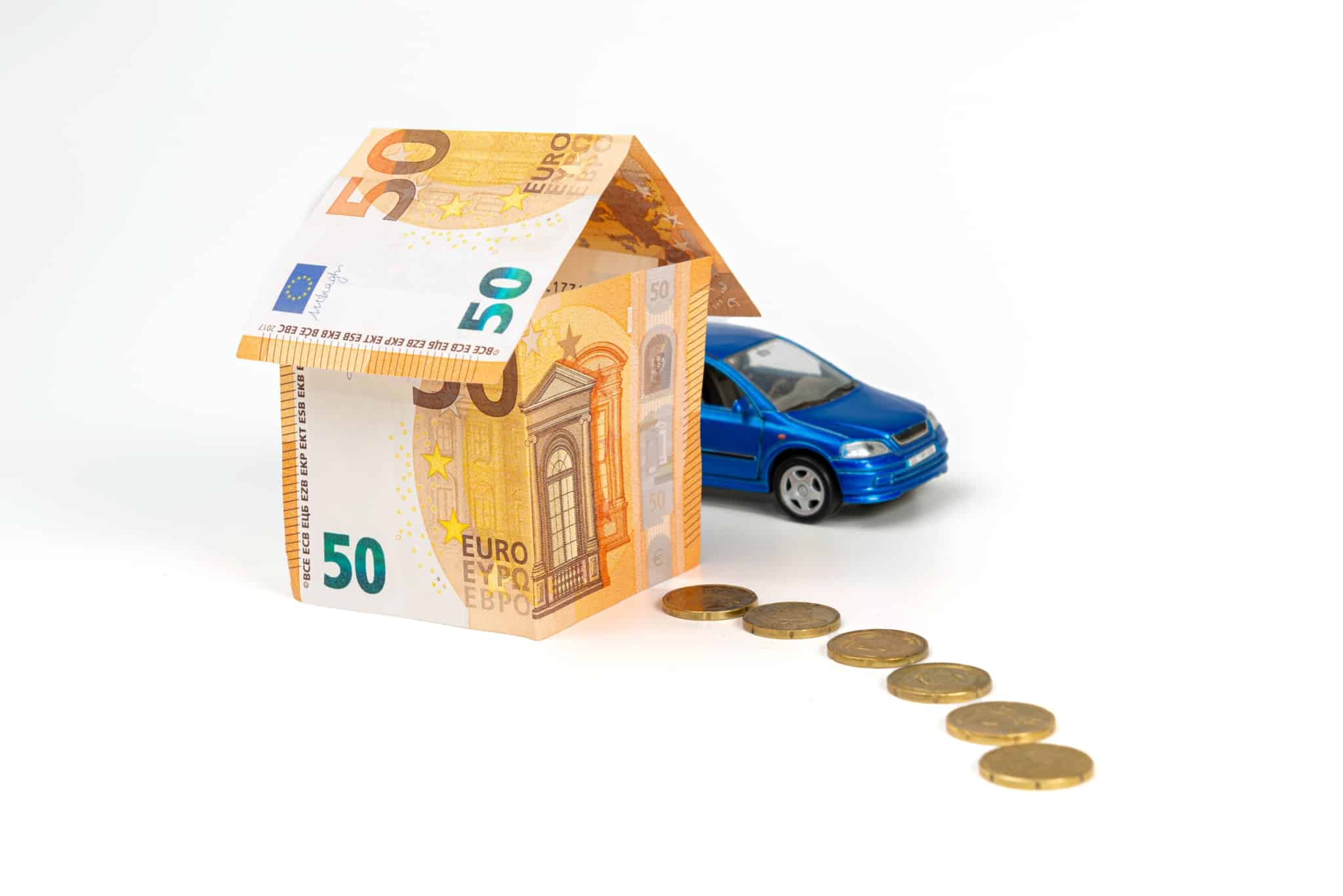 produção fotográfica com uma casinha feia de notas de 50 euros, um carrinho azul de brincar a fazer um caminho com moedas