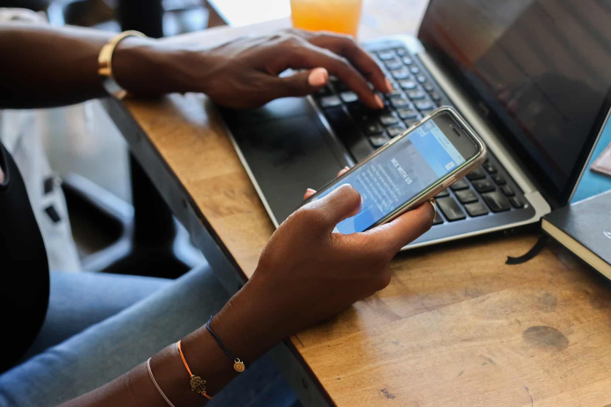 jovem mulher empreendedora consulta app no telemóvel, enquanto trabalha no seu computador portátil