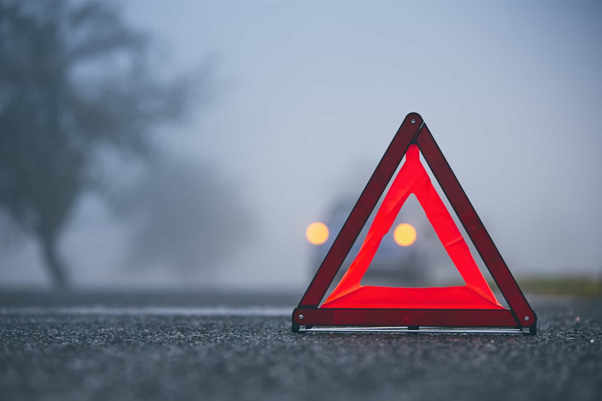 triangulo automóvel no chão, numa estrada envolta em nevoeiro, com as luzes de um carro acesas bem ao longe