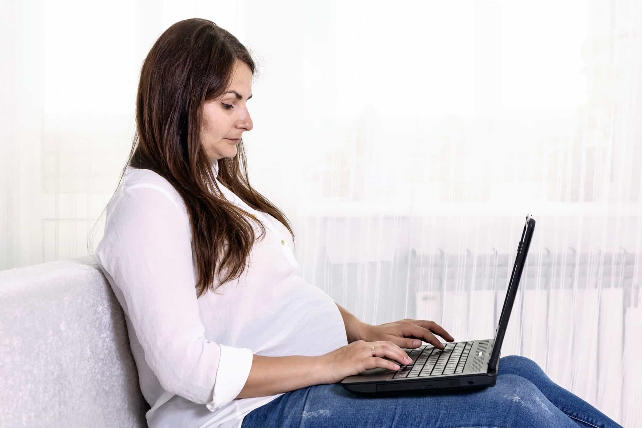 jovem mulher grávida atravalhar com o seu computador portátil no colo