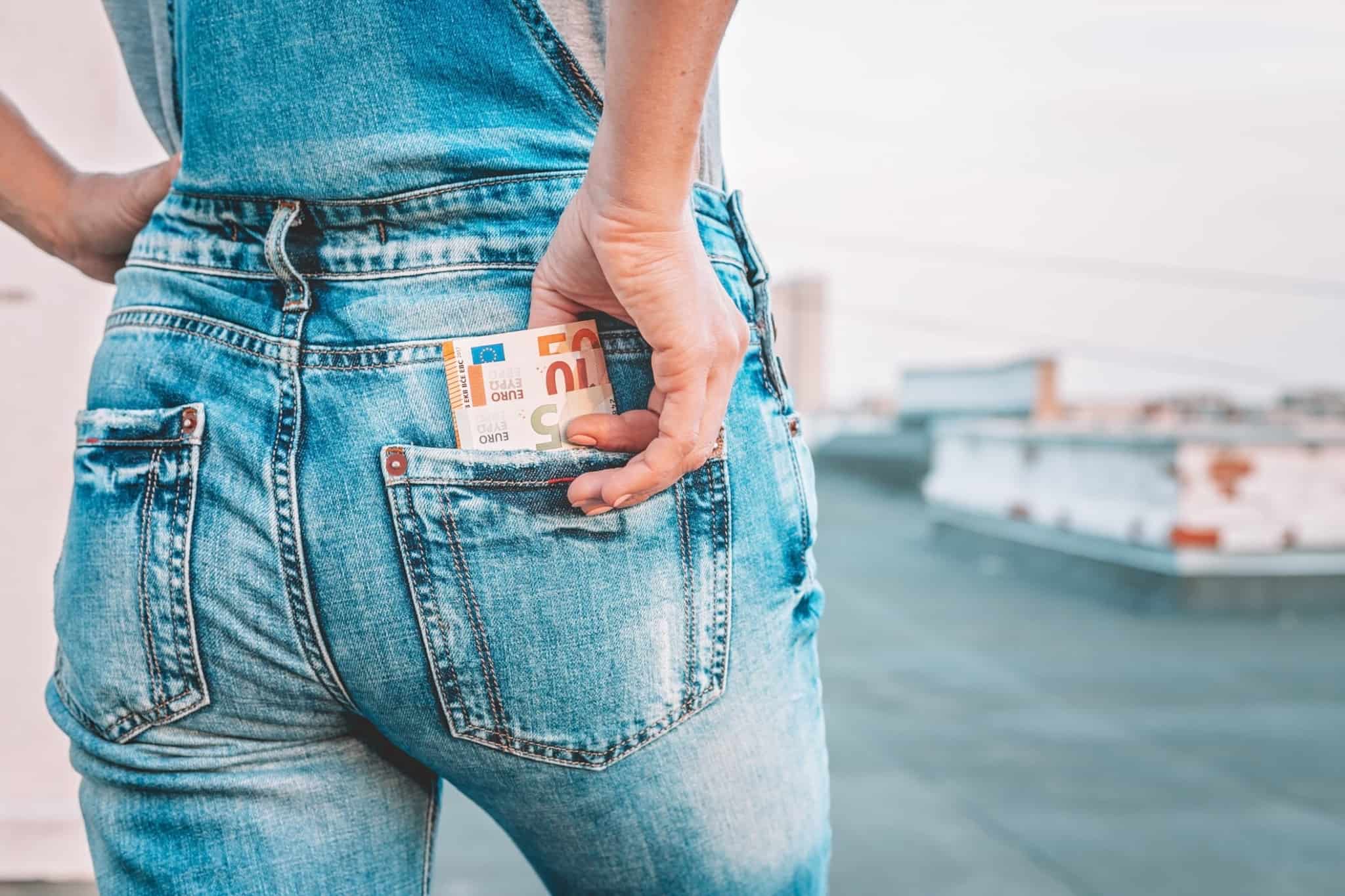 jovem mulher guarda no bolso detrás das calças de ganga algumas notas de euros