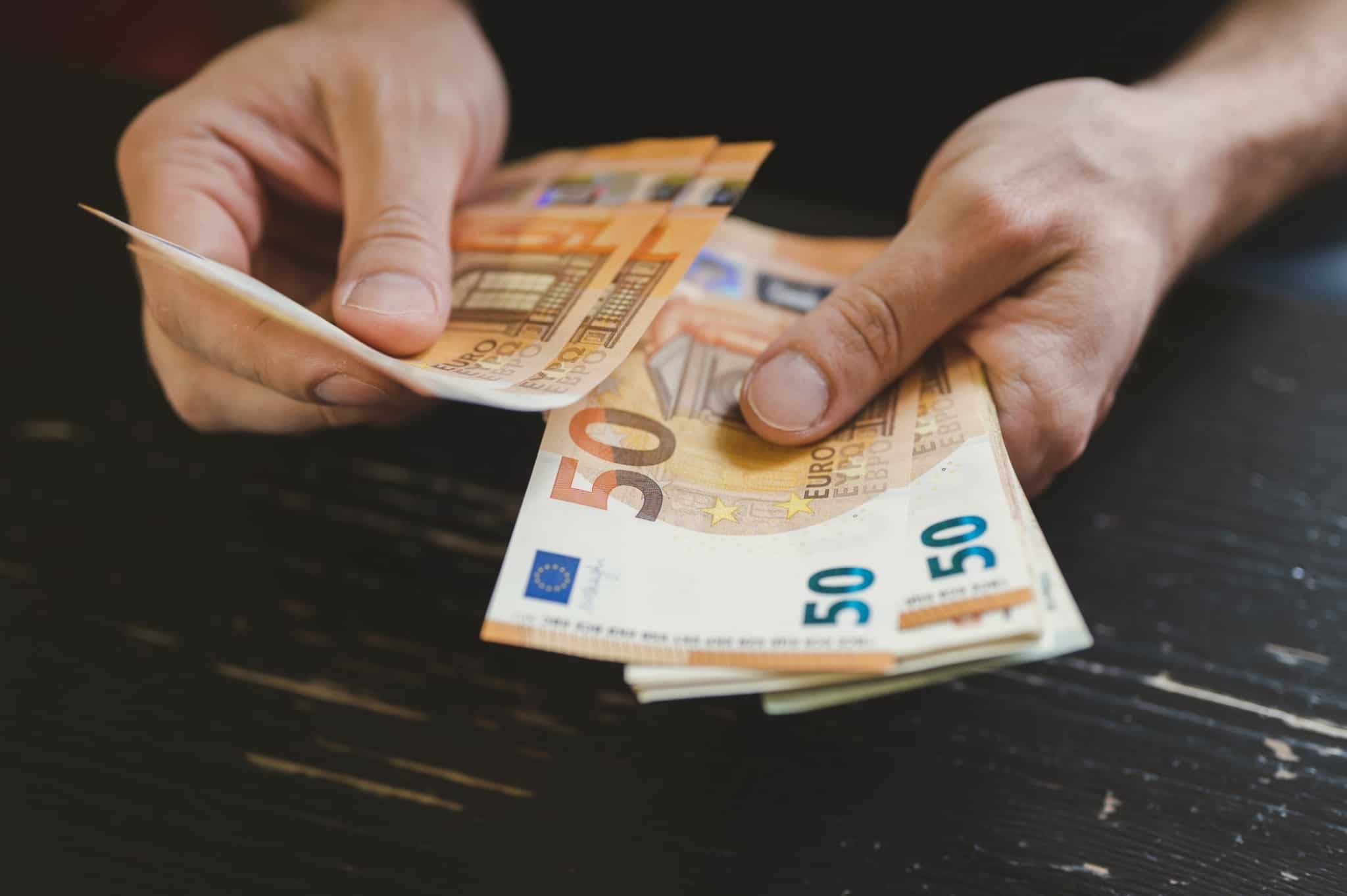 mãos de um homem jovem mostram, e contam, algumas notas de 50 euros