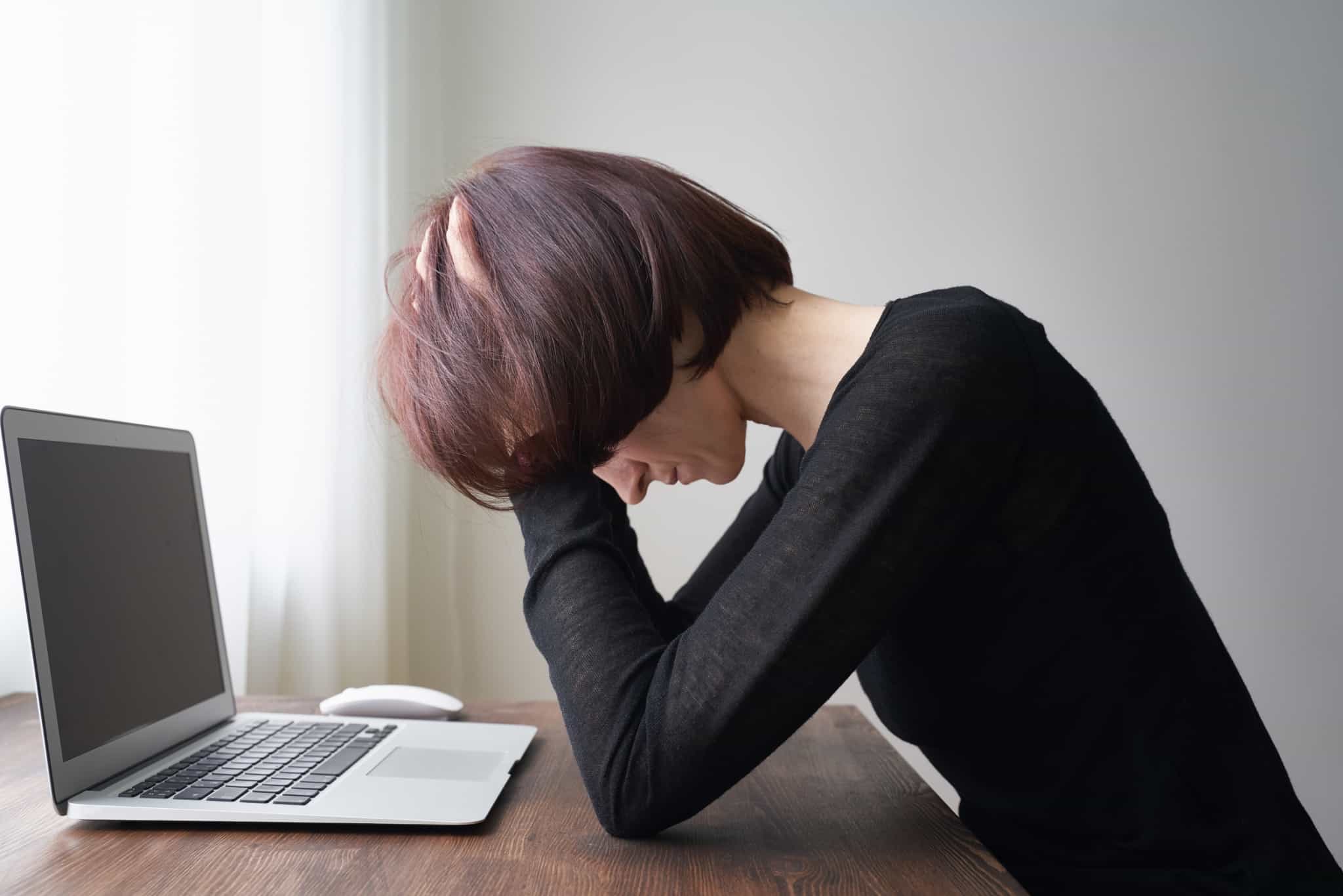 jovem mulher, exausta e de mãos na cabeça, frente ao seu computador