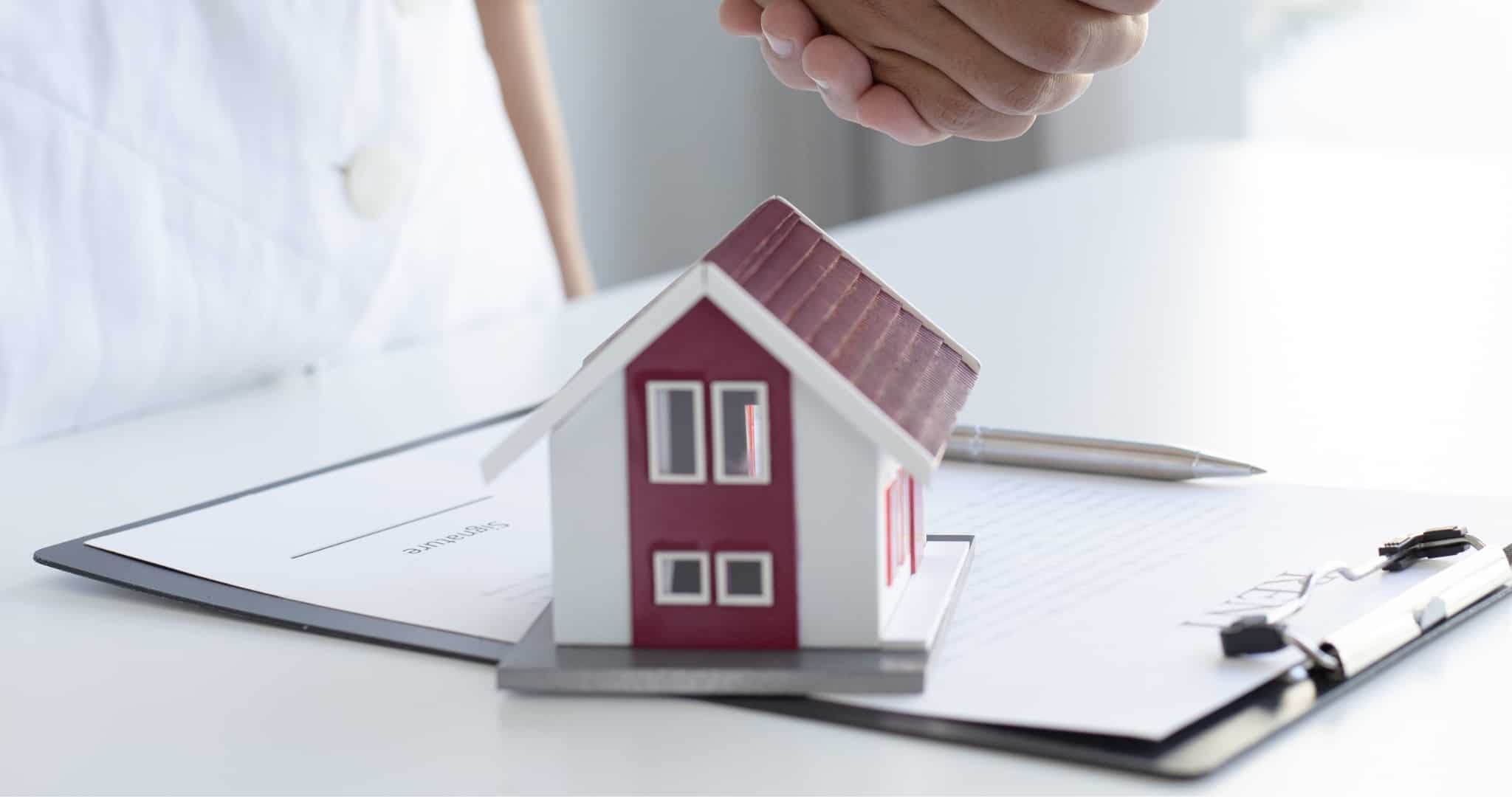 Aperto de mãos por cima de mesa com contrato e casa de madeira