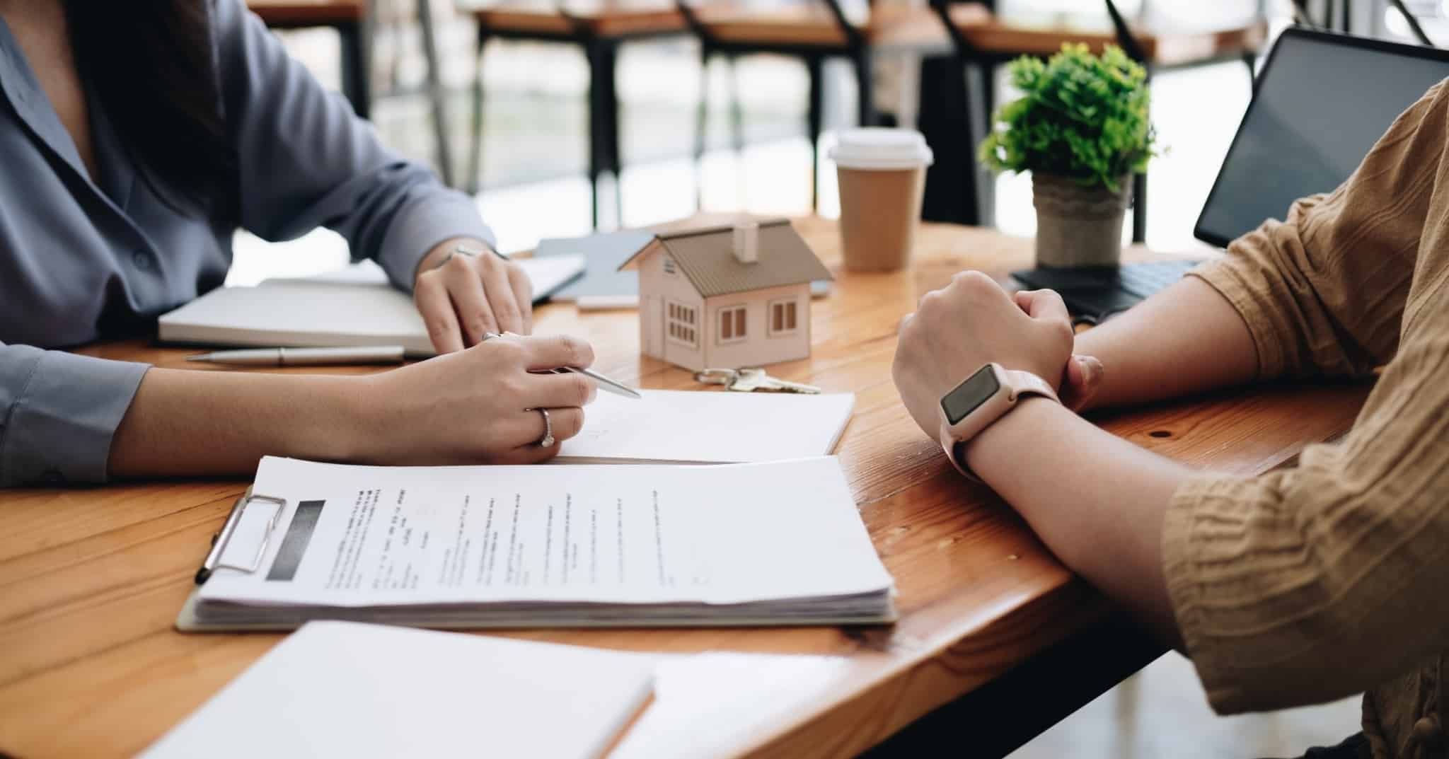 Imagem de duas pessoas numa mesa com documentos que parecem ser contratos para comprar casa - intermediário de crédito