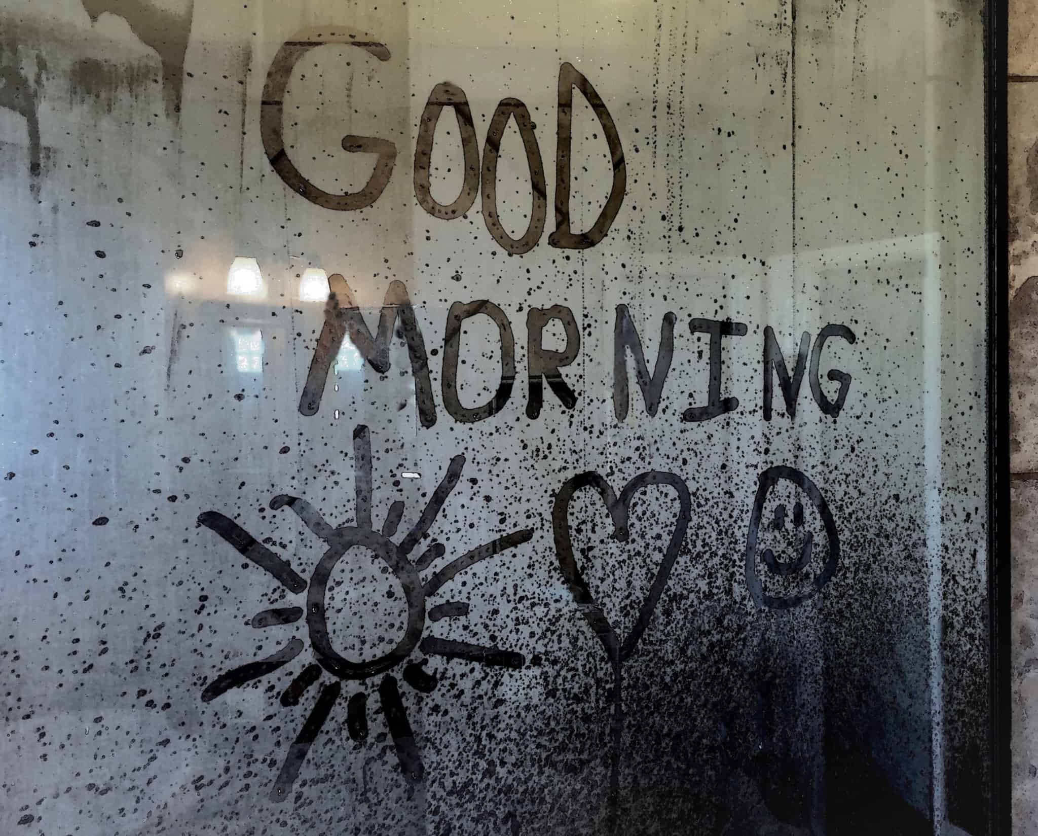 vapor da água quente no espelho da casa de banho em que foi escrito à mão e em inglês a expressão bom dia e corações e sol