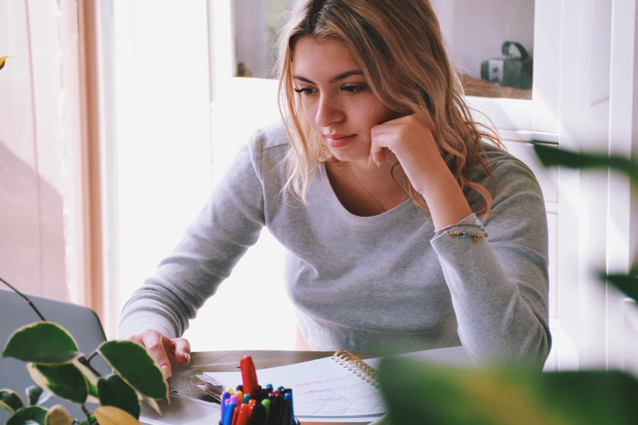 mulher jovem, com olhar apreensivo e focado, a estudar, com apontamentos no caderno e a usar o computador