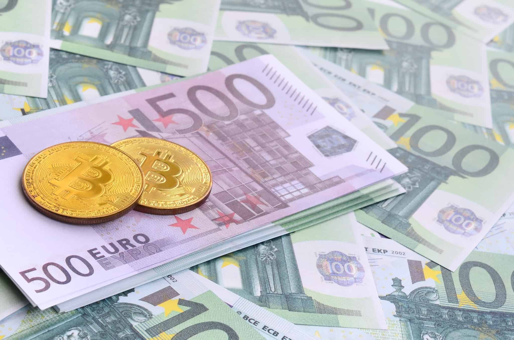 duas bitcoin em cima de algumas notas de 500 e 100 euros
